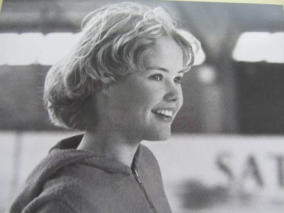 Mustavalkoinen valokuva iloisesta nuoresta naisesta, jolla on lyhyt, kihara vaaleahiuksinen kampaus, hymyilee ja katsoo oikealle.