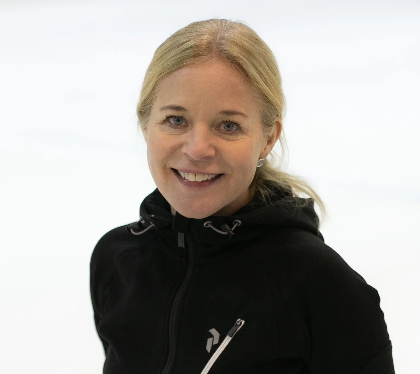Nuori nainen hymyilee kameralle, takana valkoinen tausta, pukeutuneena mustaan urheilutakkiin.