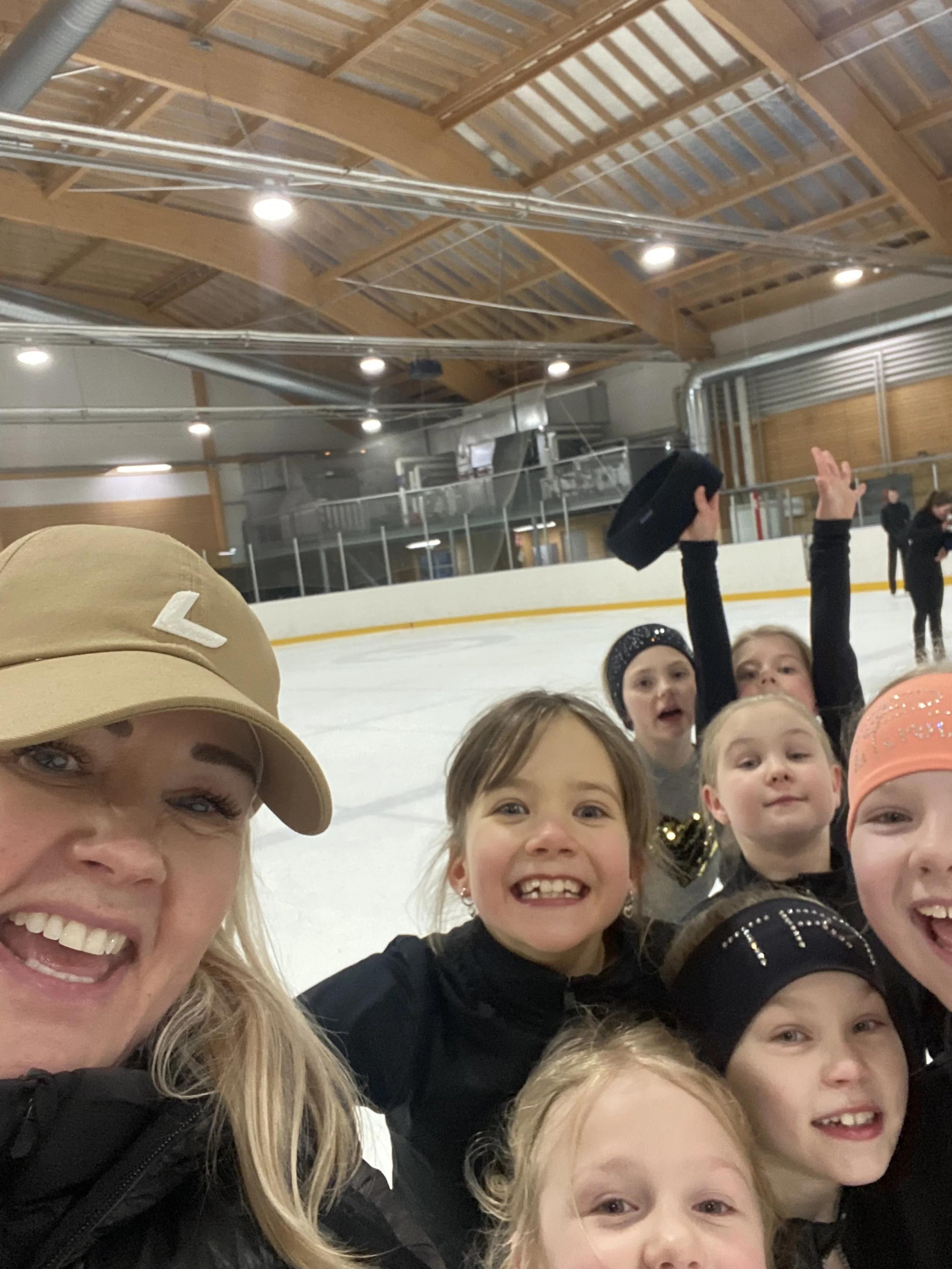 Lapsia ja aikuinen jääkiekkokaukalossa iloisina ja hymyilevinä, taustalla jääkiekkokaukalon katsomo ja katto.