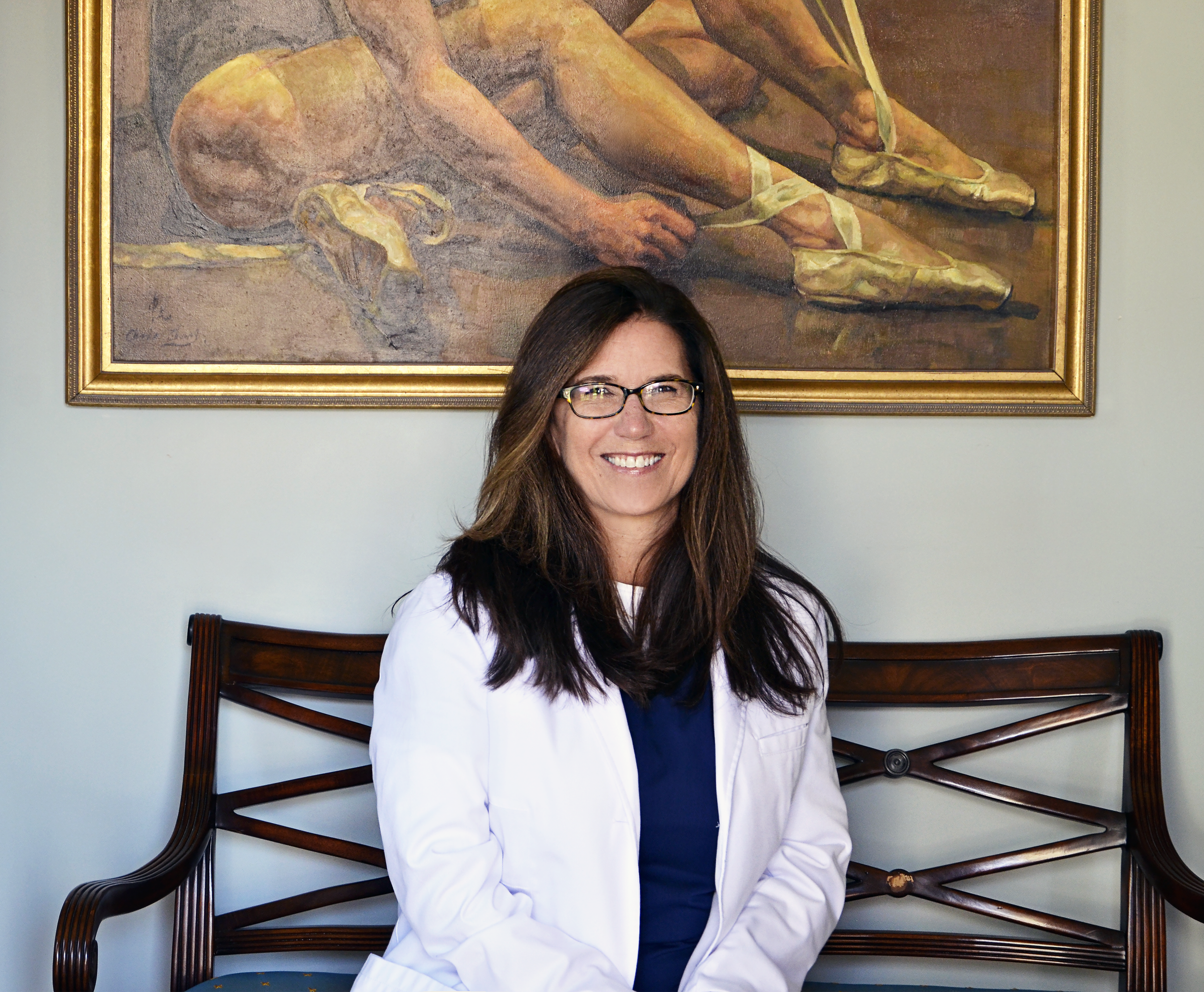 image of Dr Linda Robson seated, smiling, with ballet dancer painting in the background