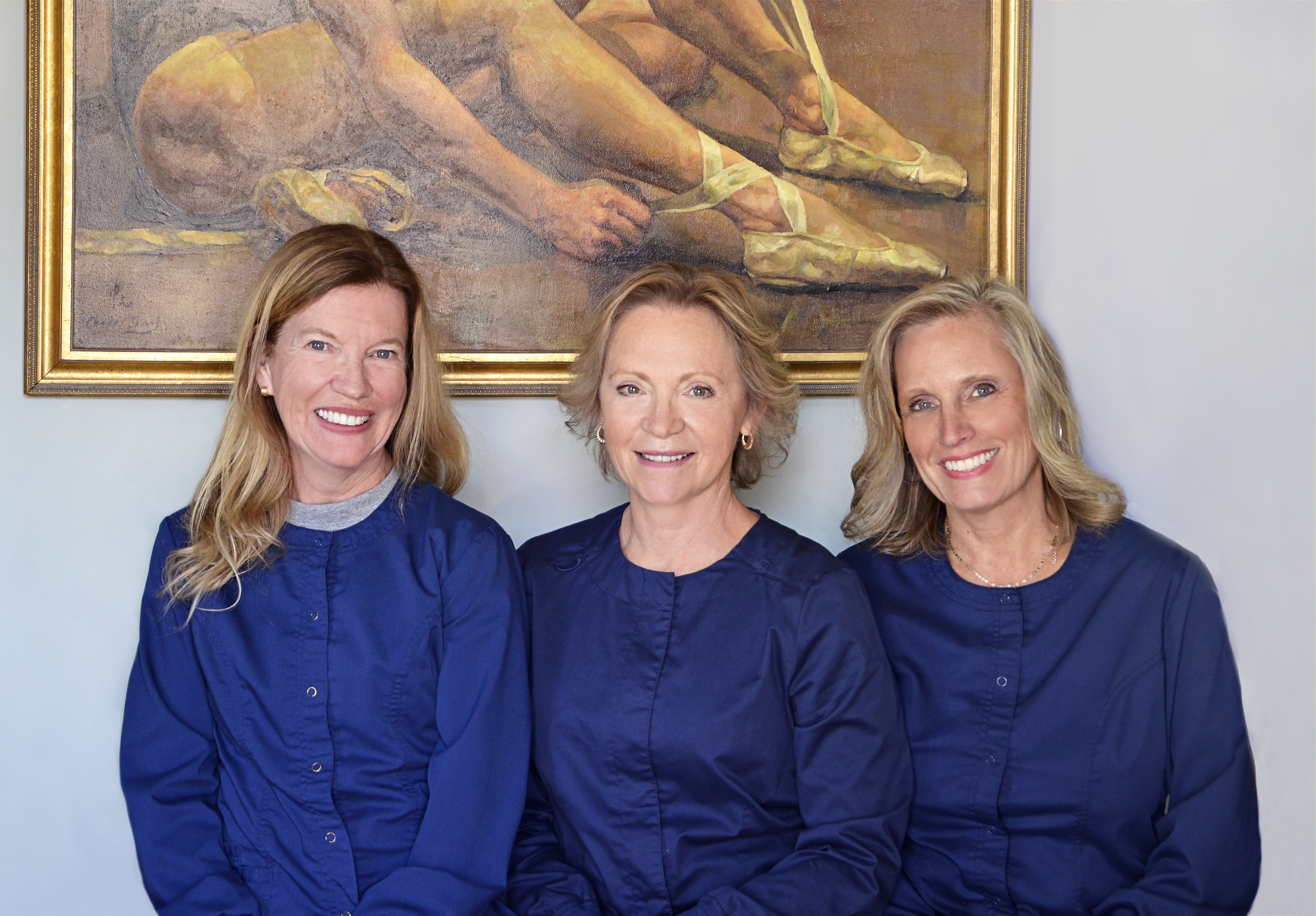 Christine, Joanne and Kim in royal blue scrubs standing in front of dancer painting in gold frame