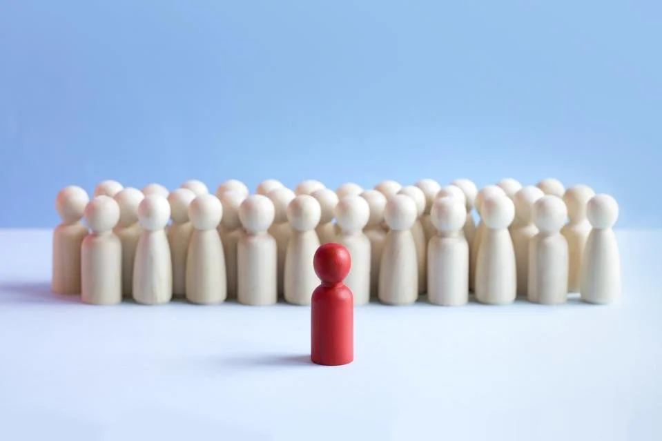 A red game piece stands in front of a group of white game pieces, all arranged on a light blue background.