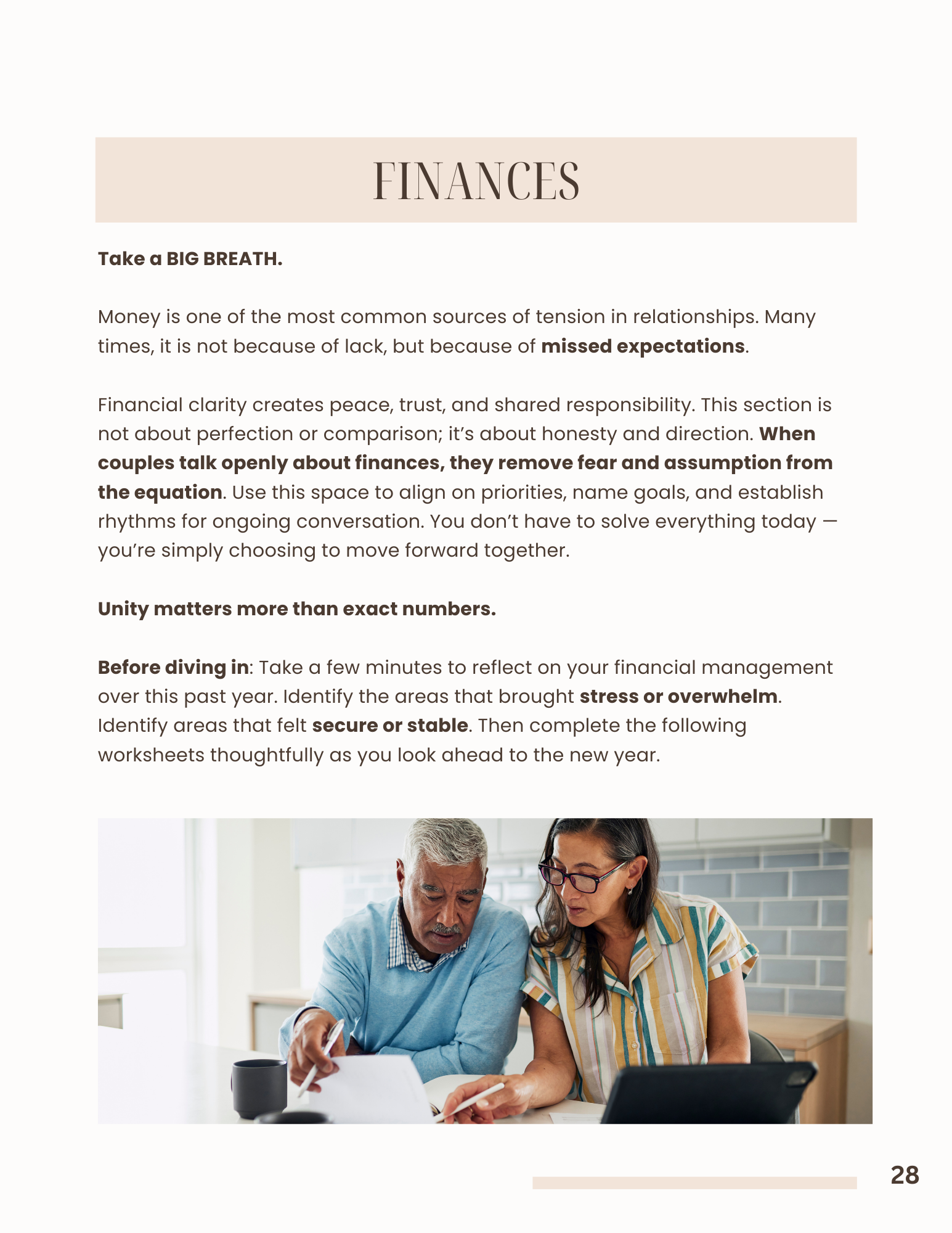 Two older adults, a man and a woman, sit at a table reviewing documents together in a bright room.