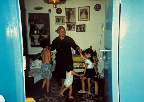 A woman dancing with four children in a cozy living room, decorated with framed photos and various decor items on the wall.