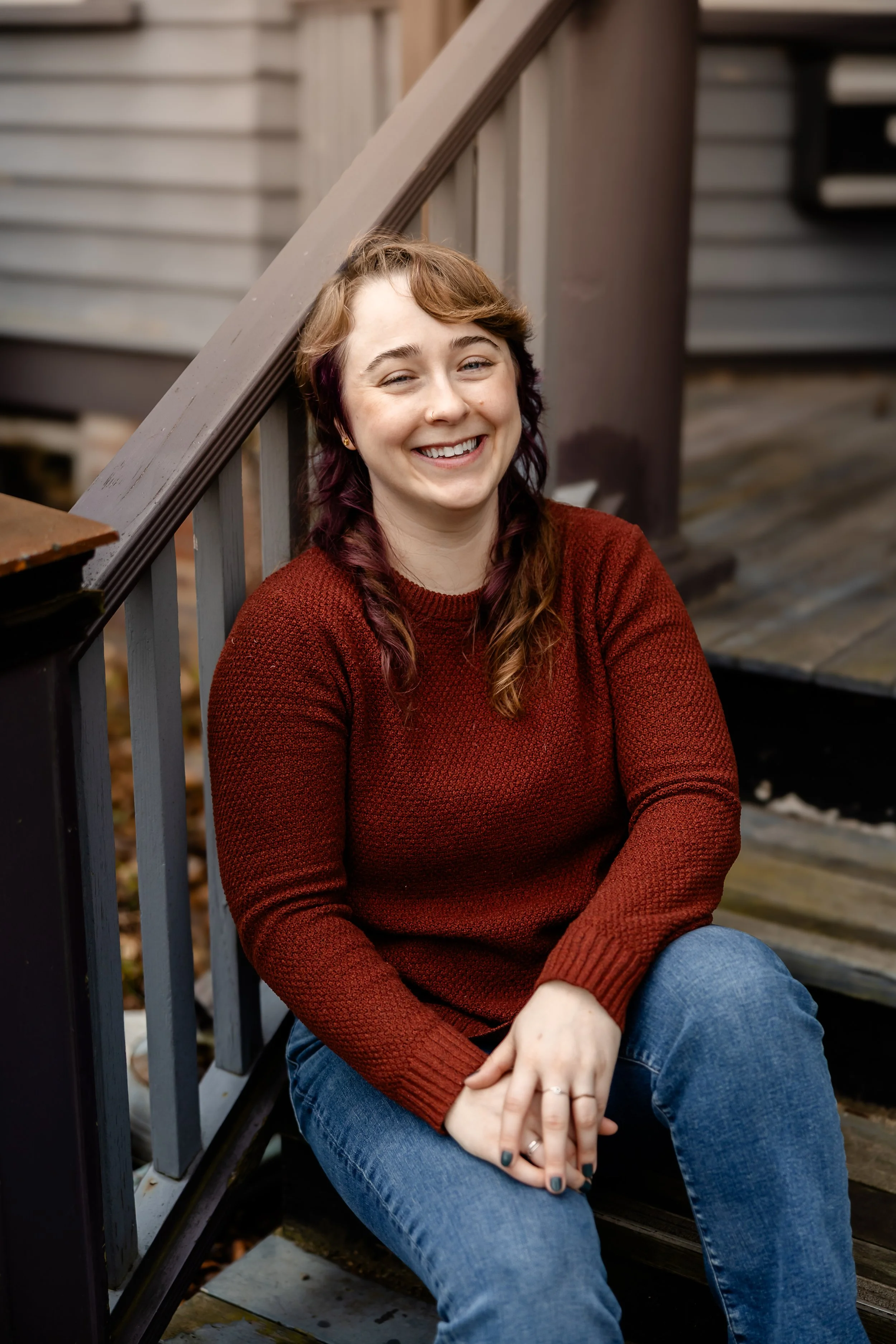 white person long brown and purple hair sitting on stairs, smiling. cambridge & boston based doula