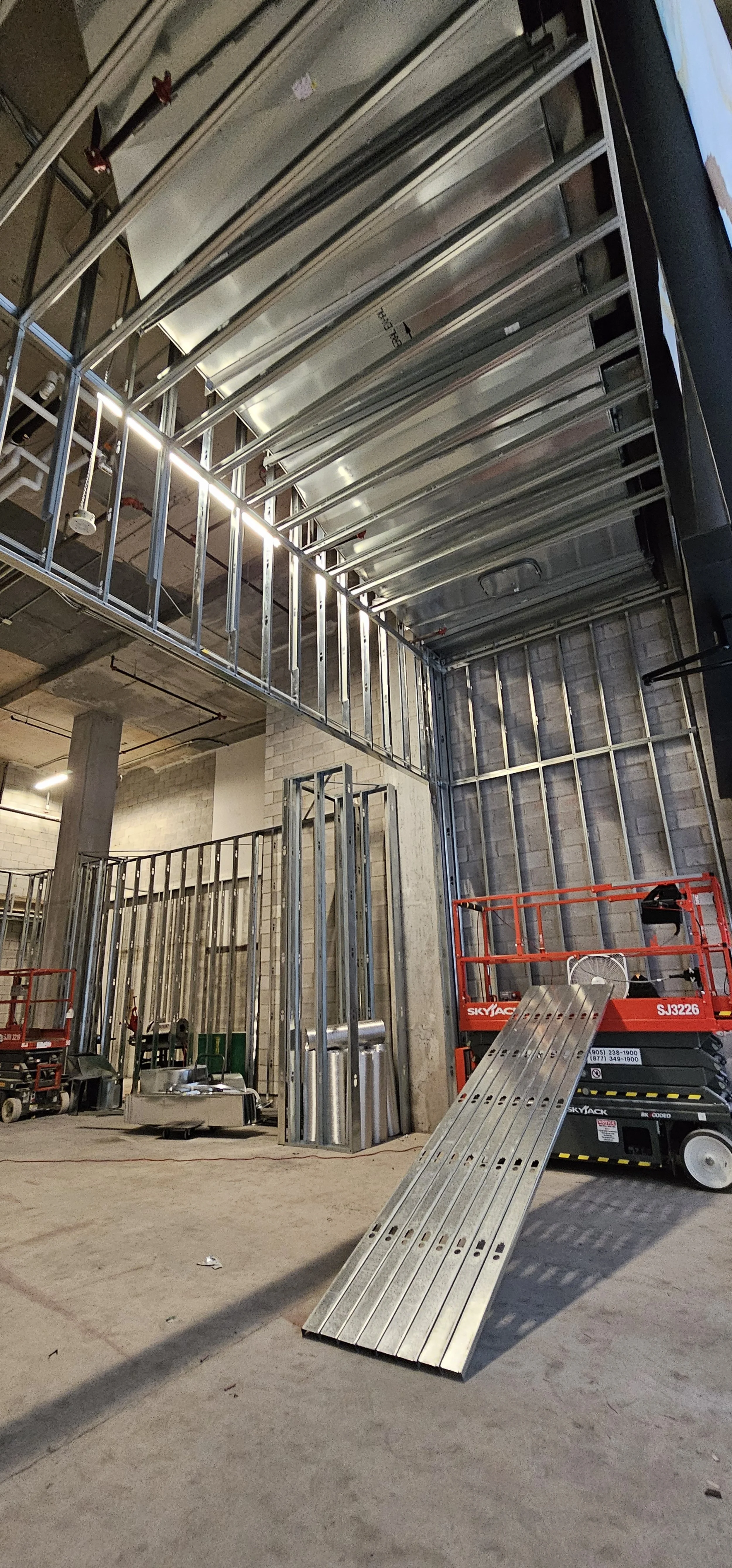 Construction site with steel framing and scaffolding for building interior, with scissor lift equipment nearby.