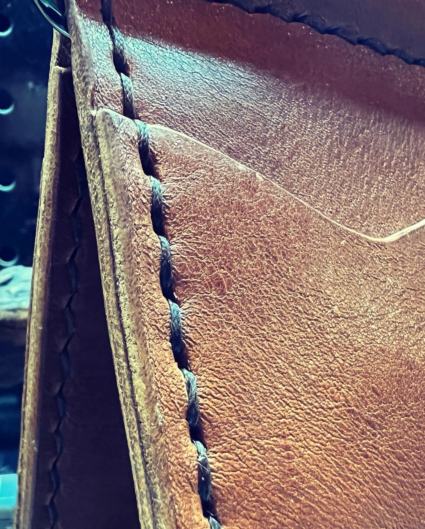 Close-up image of the stitched edge of a brown leather item, showcasing the textured surface and detailed stitching.