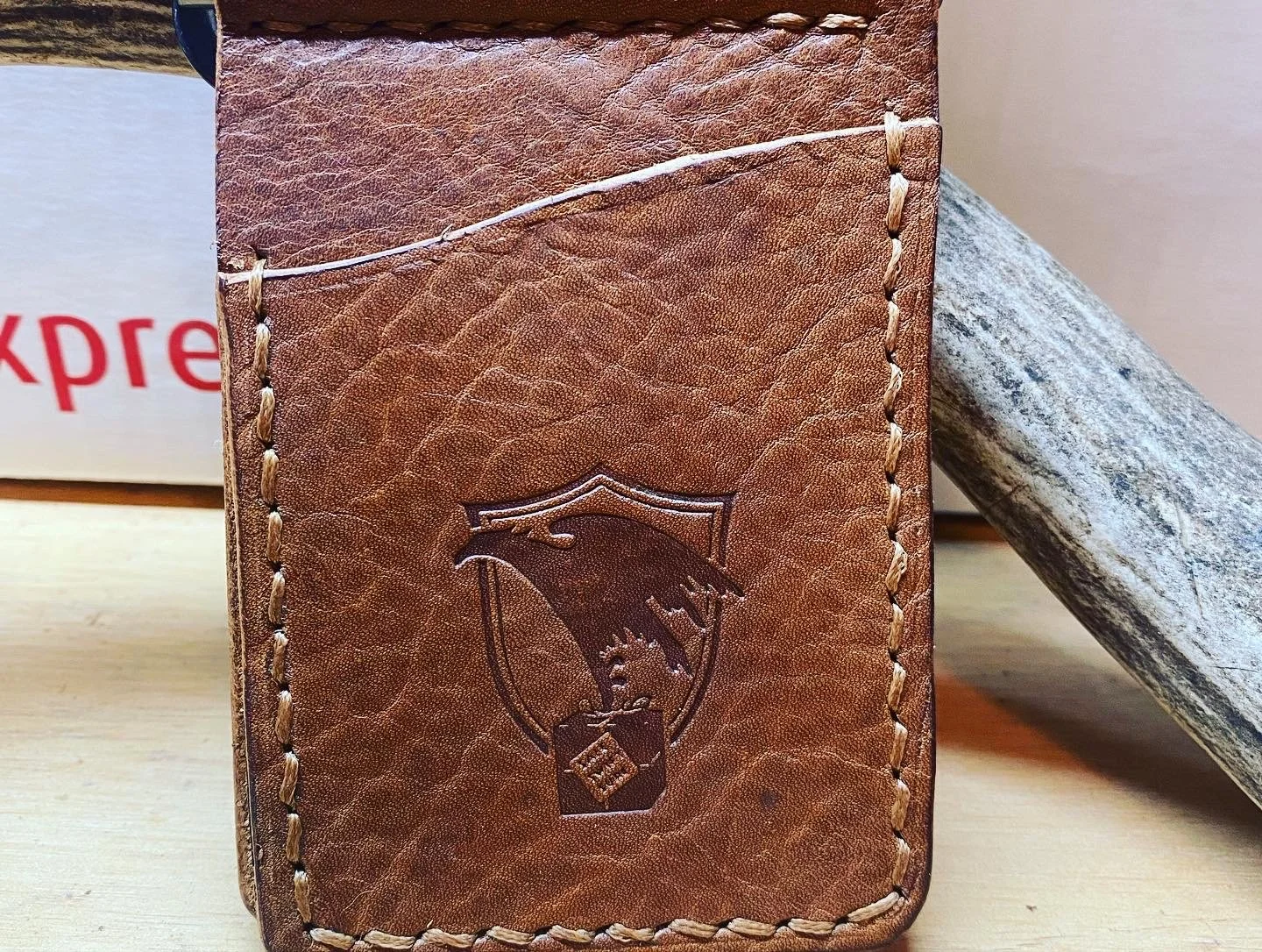 Close-up of a brown leather wallet with a shield emblem and a dragon design embossed on it, stitched with white thread.