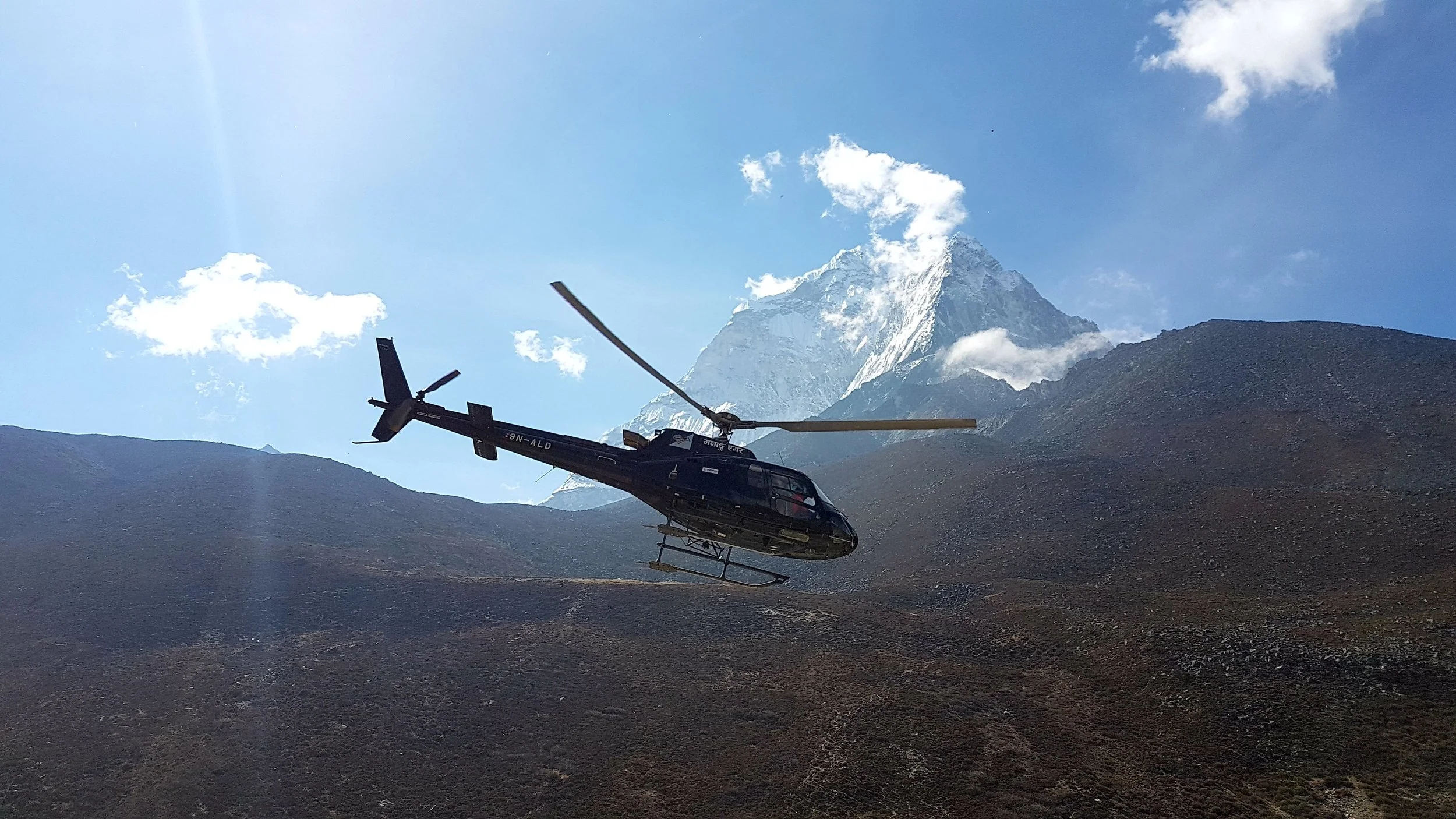 A helicopter flying in the mountains with a snow-capped peak in the background.