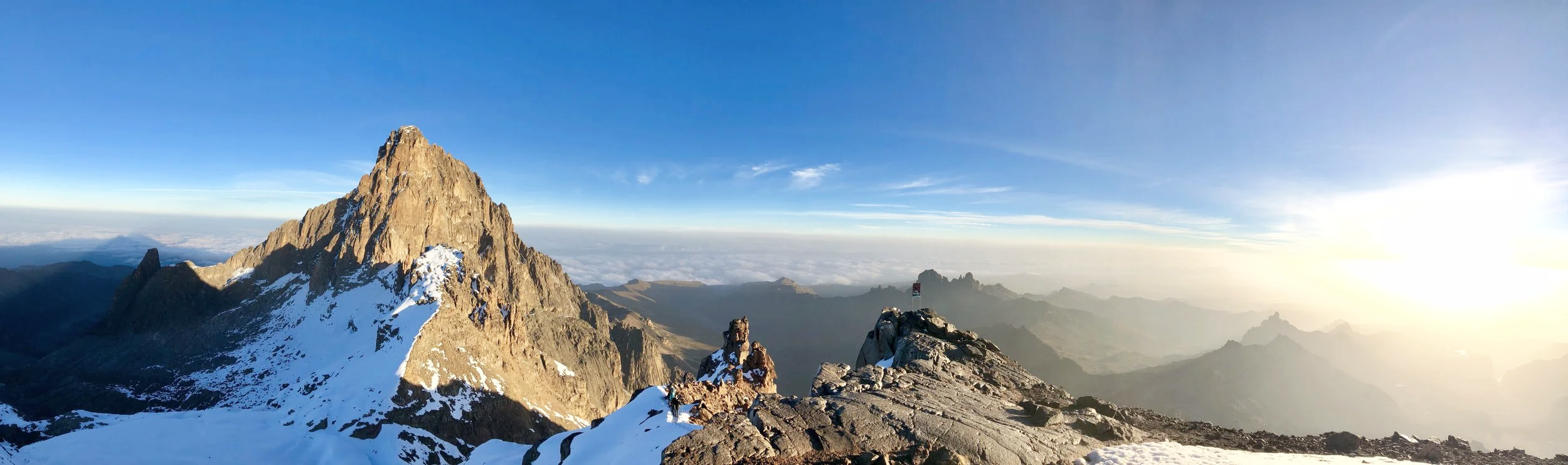 Mountain peak with snow, rocky ridges, and a clear blue sky during sunrise.