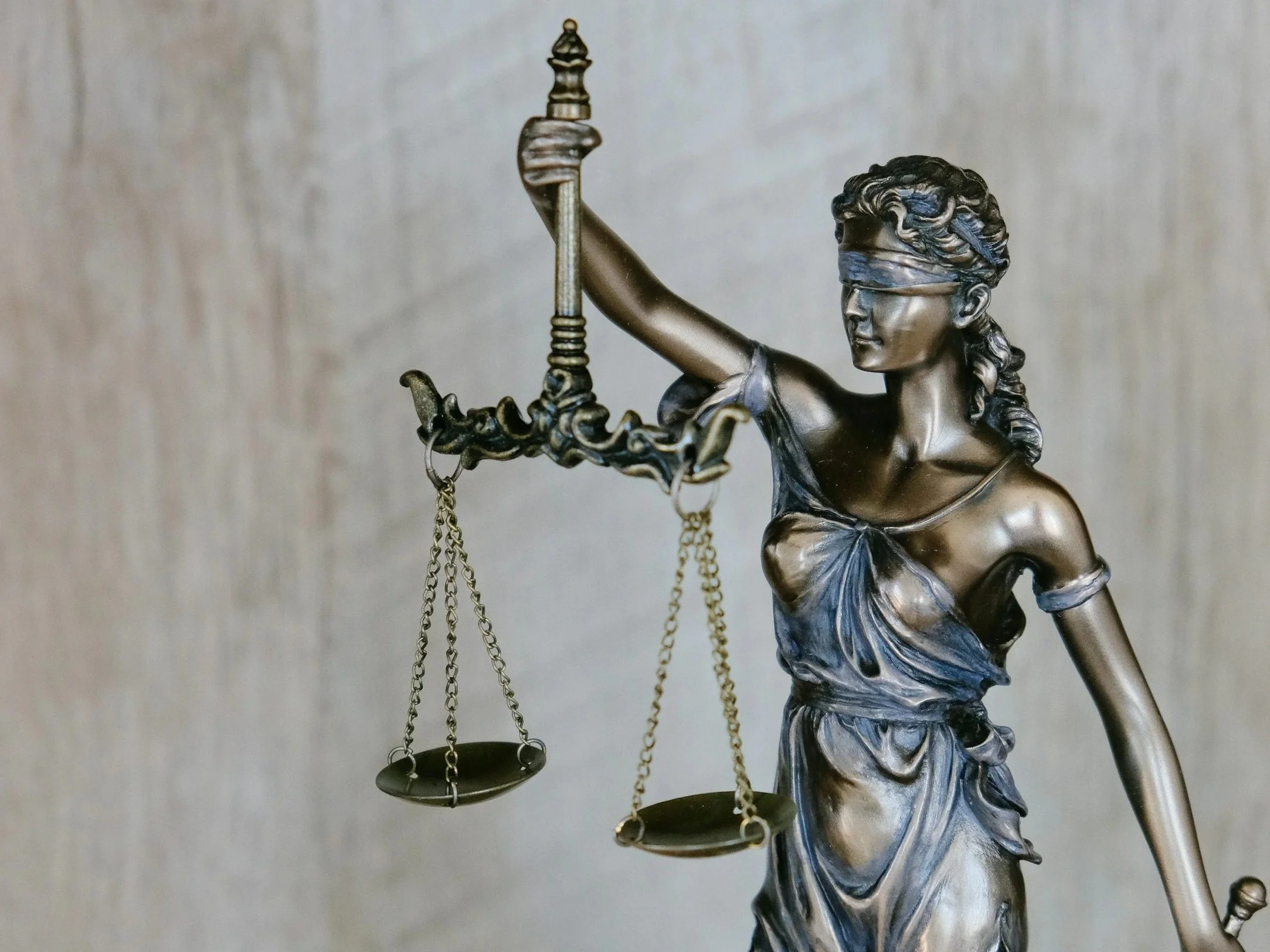 Close-up of a metallic statue of Lady Justice with a blindfold, holding a set of balance scales in her right hand.