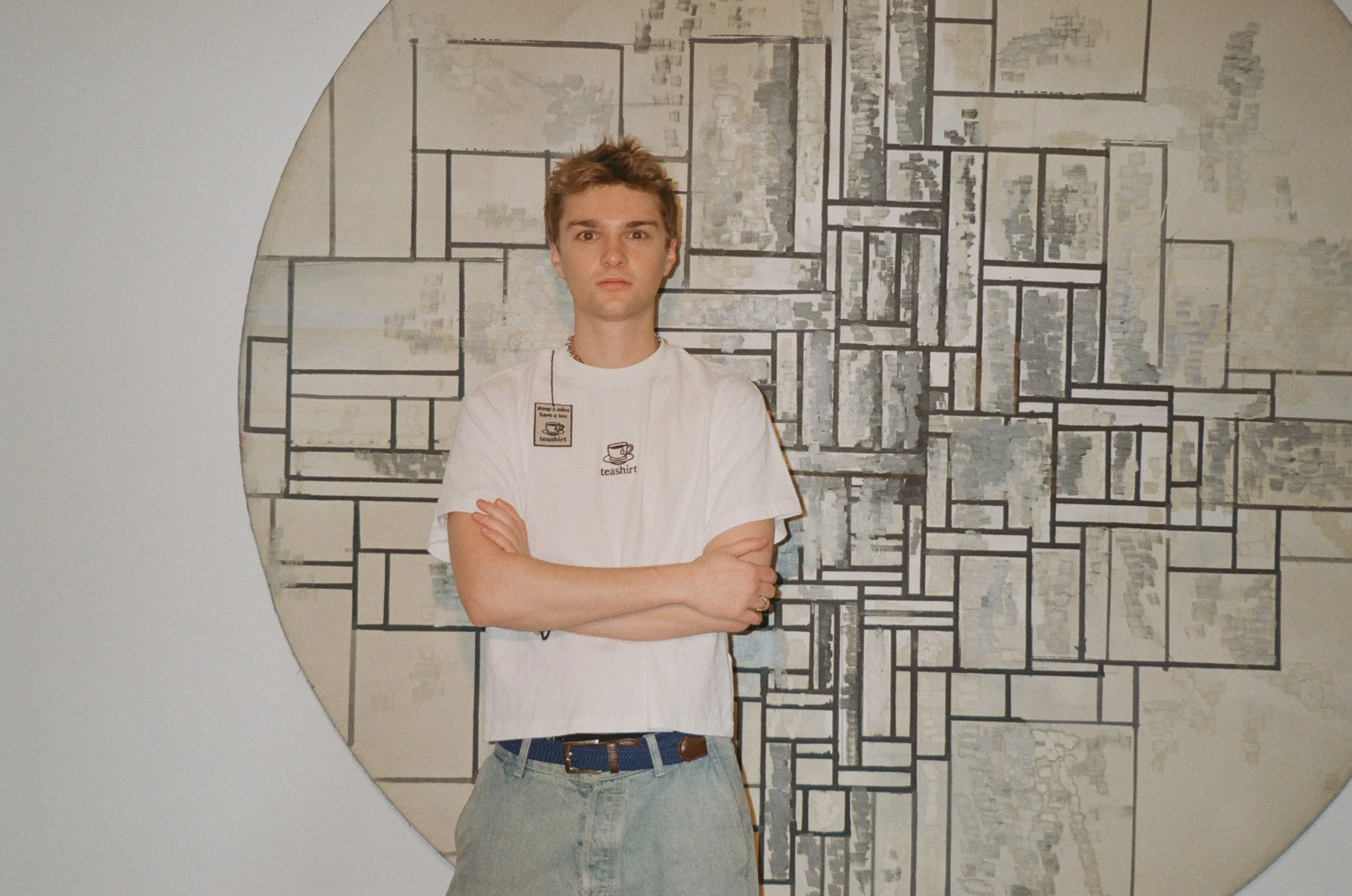 Young man with crossed arms standing in front of an abstract geometric wall art piece.