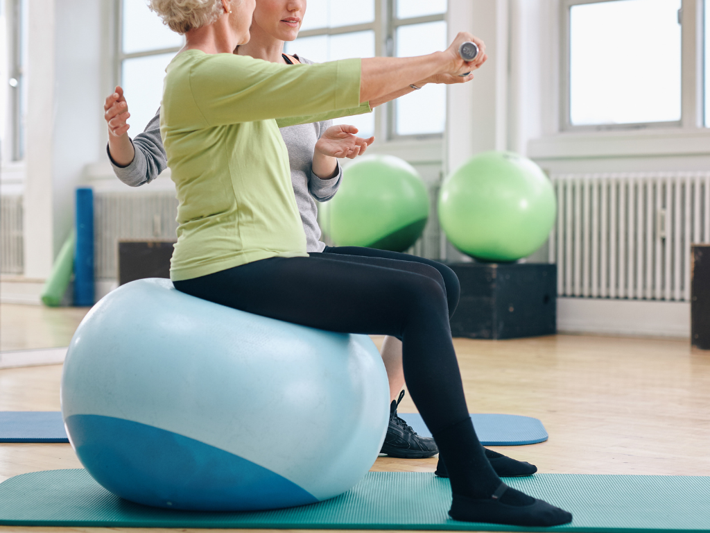 Functional Movement Specialist helping woman on a yoga ball with weighted exercise
