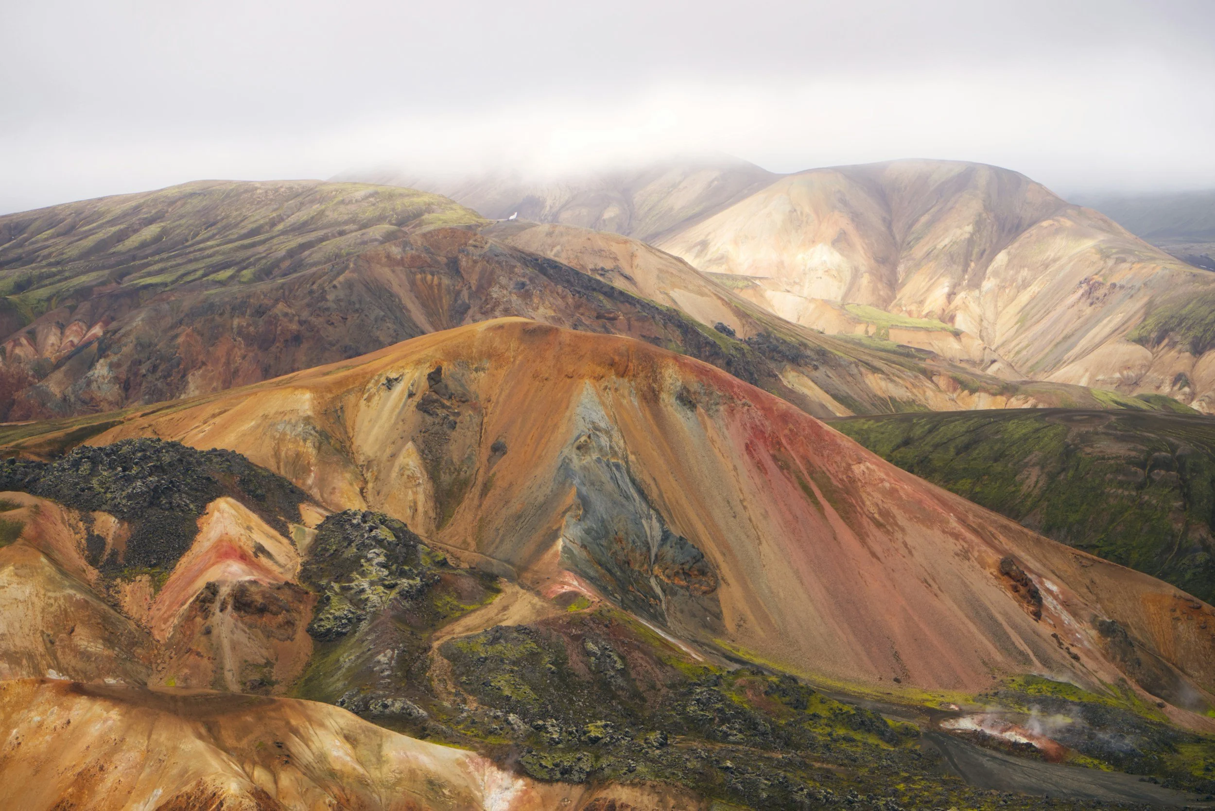 Colorful mountain landscape with multicolored ridges and patches of green moss.