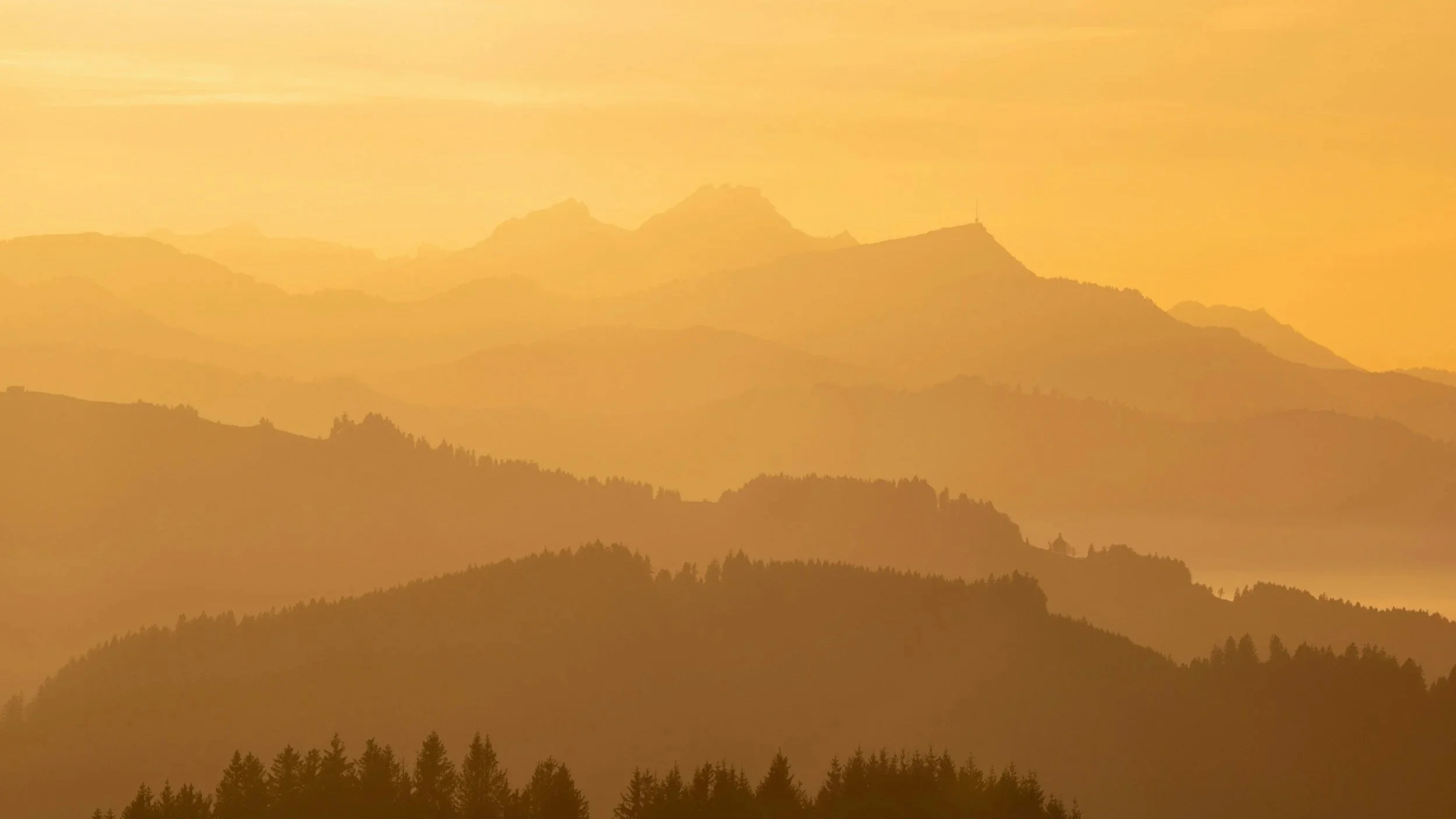 Sunset over a layered mountain range with a warm, orange glow.