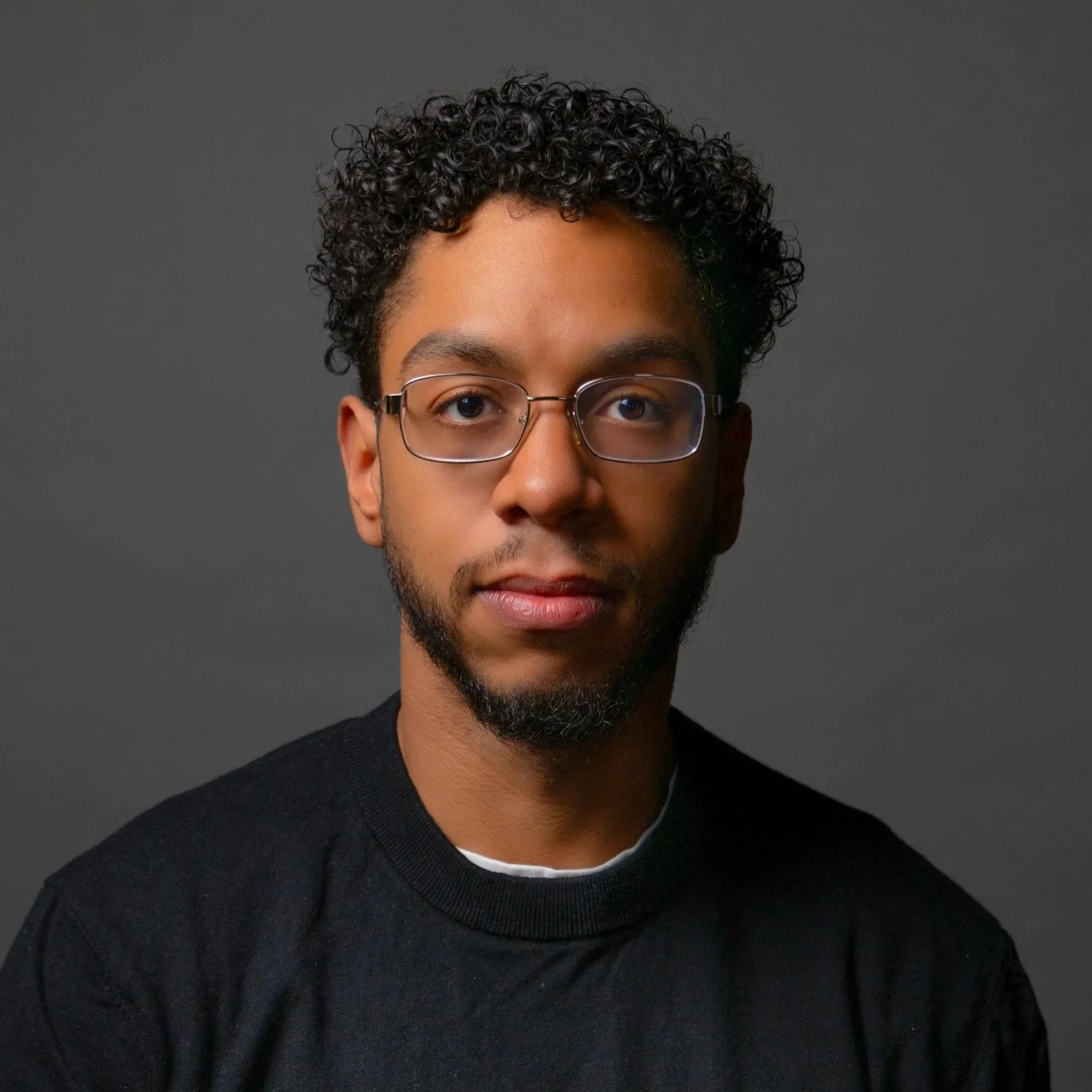 Young man smiling outdoors at event with buildings, stage, and equipment in the background