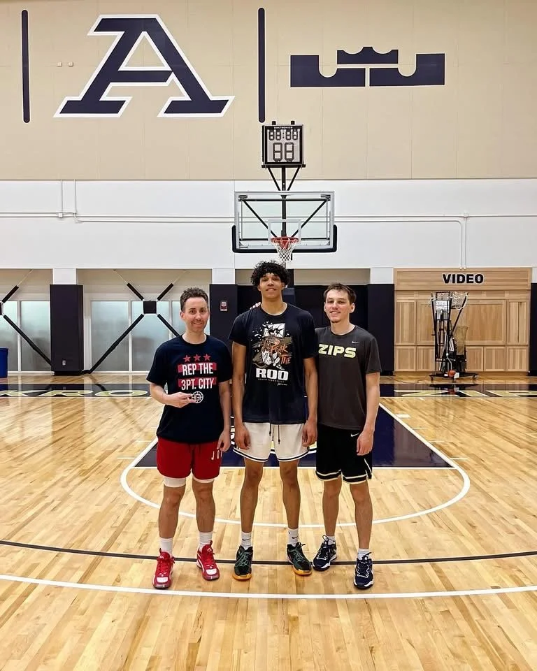 Three young men standing on a basketball court posing for a photo.
