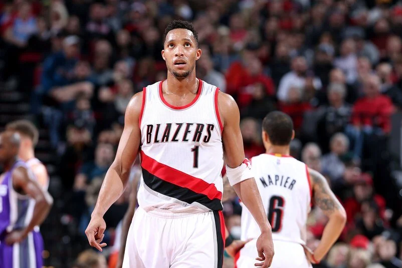 An NBA player in a Blazers uniform on the court during a game, with a crowd in the background.