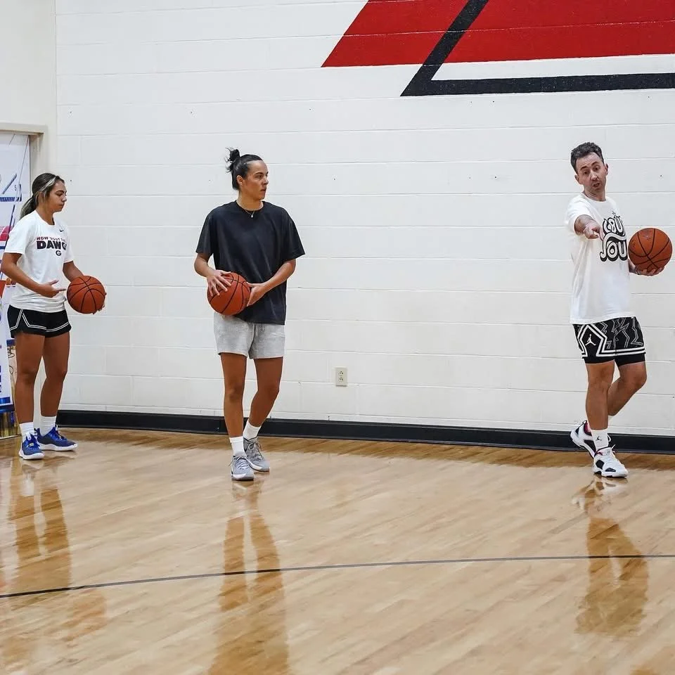 Three people holding basketballs in a gym, practicing dribbling drills.