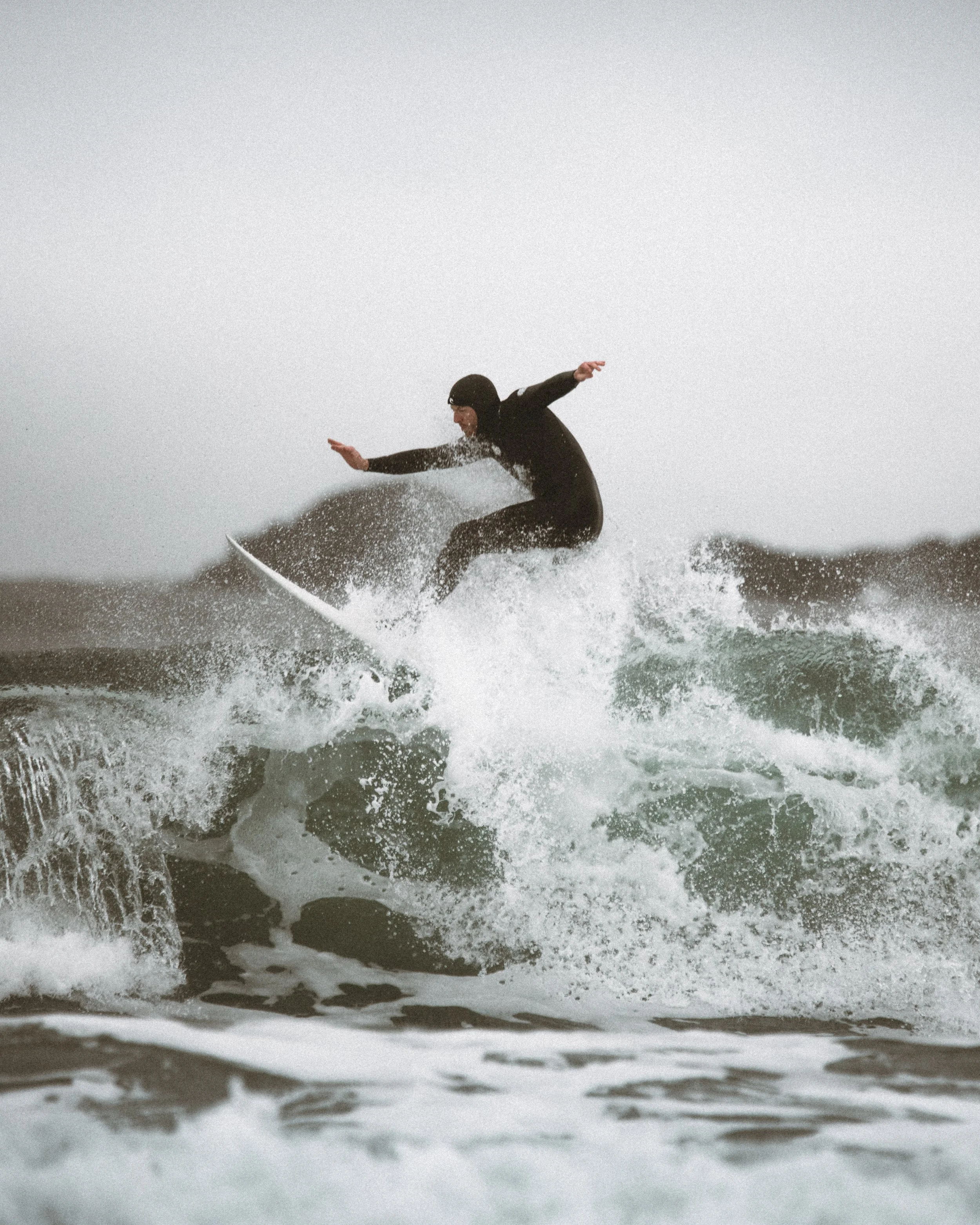 A person in a wetsuit and helmet riding a wave on a surfboard in the ocean.