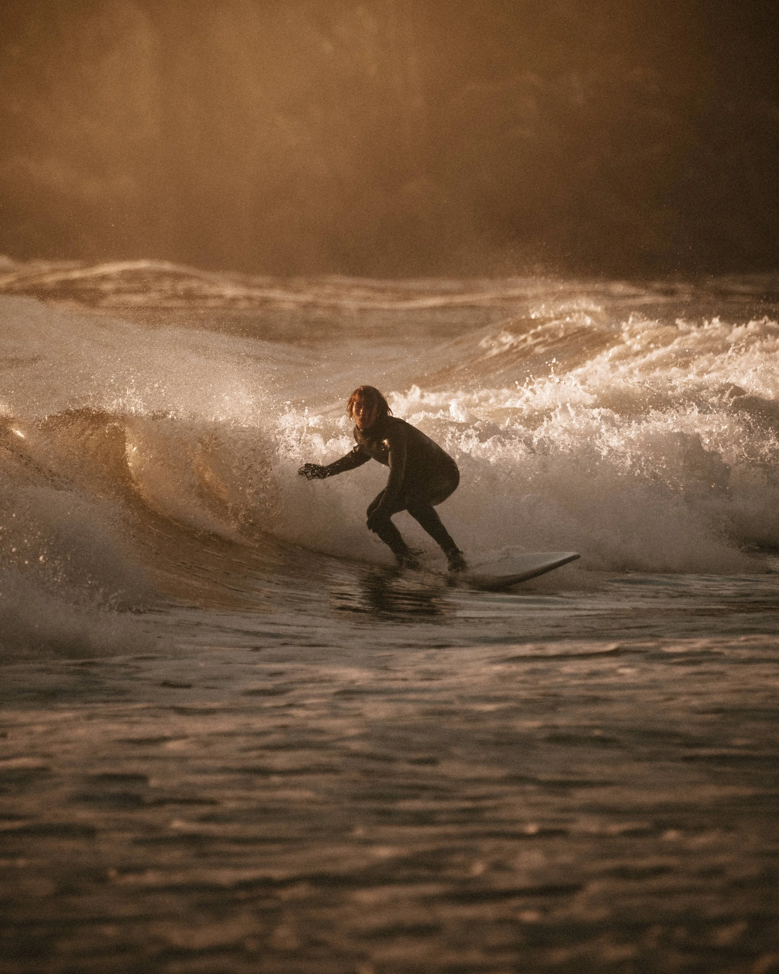 A person surfing on a wave during sunset or sunrise with a cloudy sky.