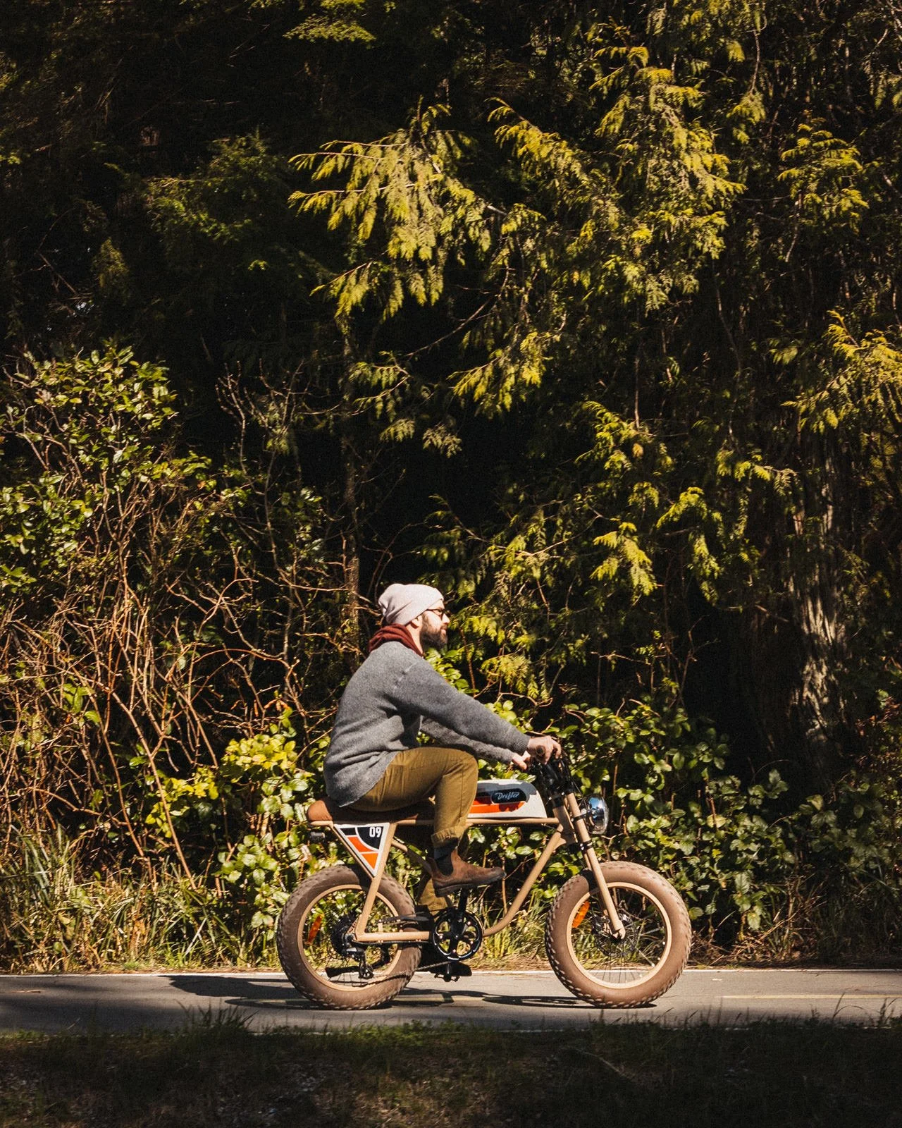 A man riding an electric fat tire bike on a paved trail surrounded by dense green trees and foliage during daytime.