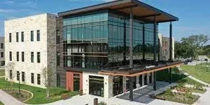Modern building with glass facade and stone walls, featuring a flat roof and surrounded by greenery.
