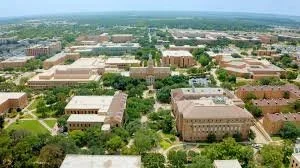 Aerial view of a university campus with multiple brick buildings, green lawns, and trees.