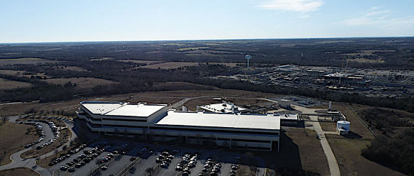 Large commercial building with a parking lot, surrounded by an expansive landscape and distant water tower.