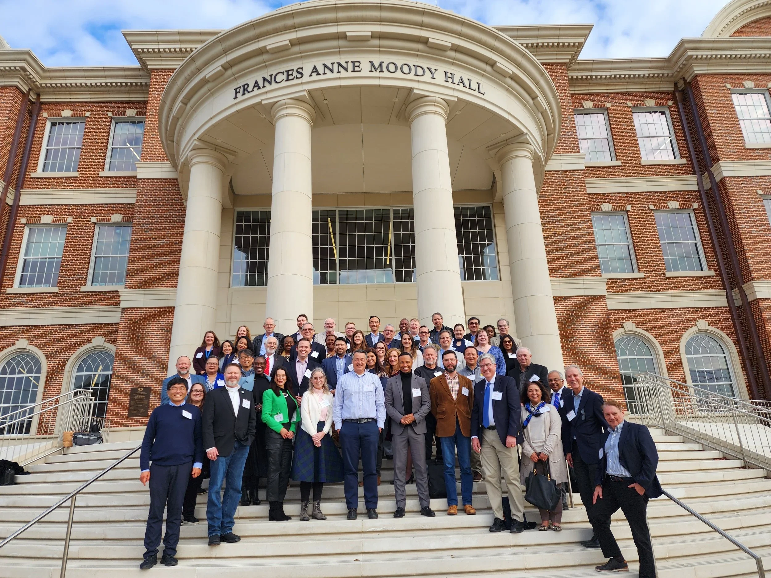 Group photo of people standing on the steps outside Frances Anne Moody Hall, a large brick building with white columns and multiple windows.