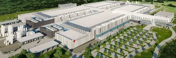 A large modern industrial or commercial complex with multiple interconnected white and gray buildings surrounded by trees and a parking lot.