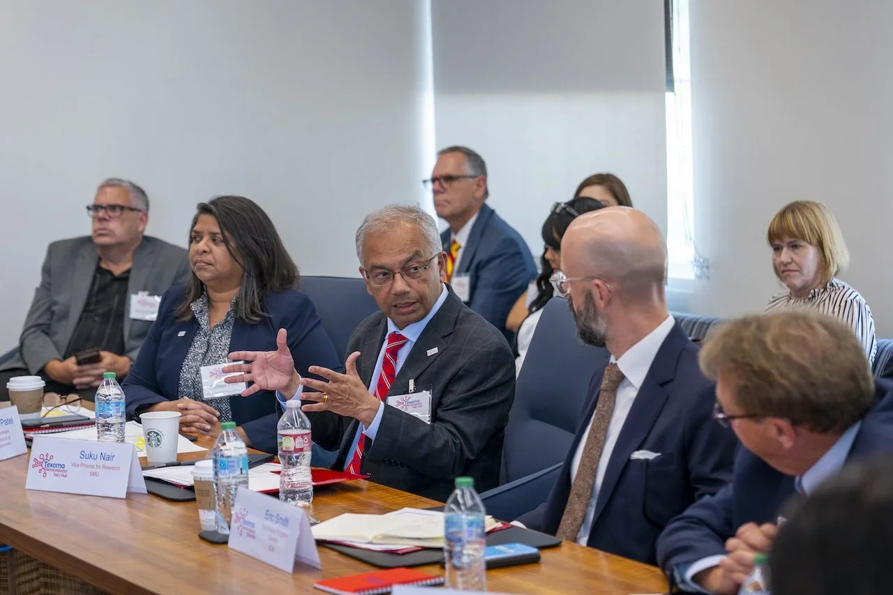 A group of diverse professionals sitting around a conference table during a meeting, with one person speaking and others listening.
