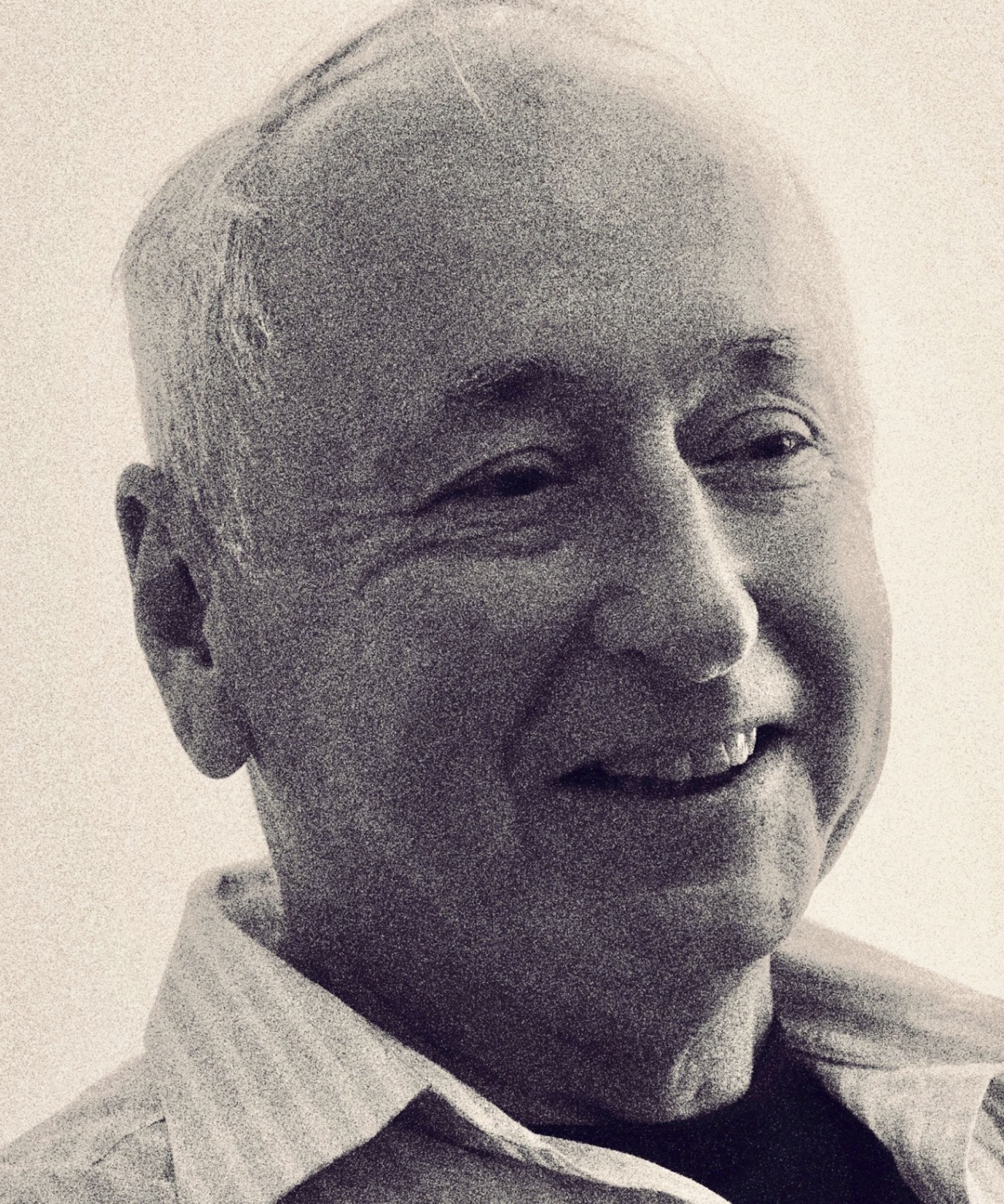 A smiling elderly man with short white hair, wearing a collared shirt.