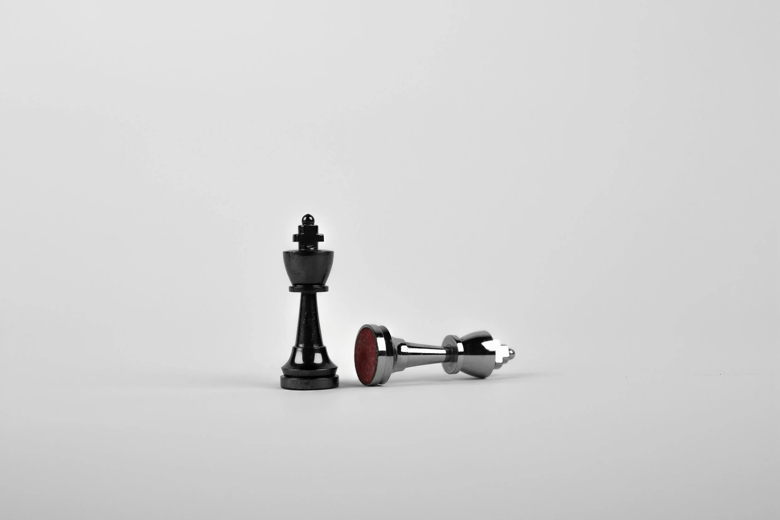 Two black chess pieces, a king standing upright and a fallen pawn, on a plain white background.