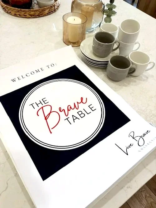 A welcome sign for a prayer table placed on a white marble table, surrounded by cups, a candle, and a small decorative item.
