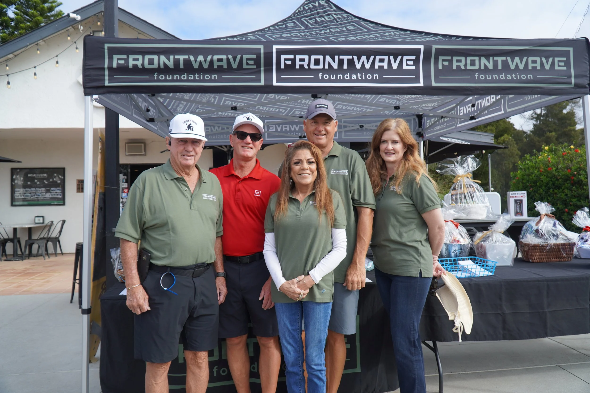 Five people standing in front of a tent with the text "Frontwave Foundation" on it at an outdoor event.