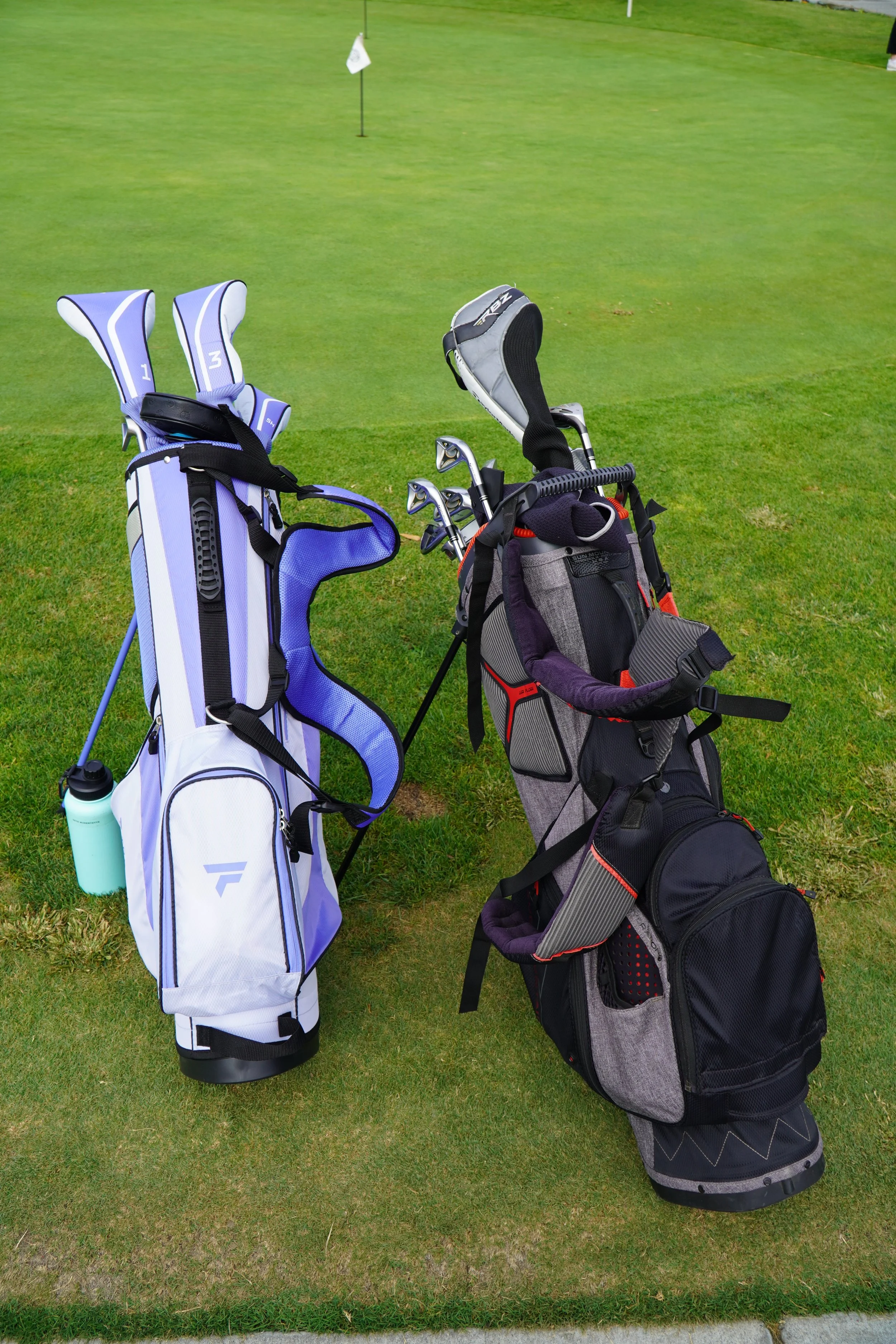 Two golf bags with clubs placed on the grass of a golf course.