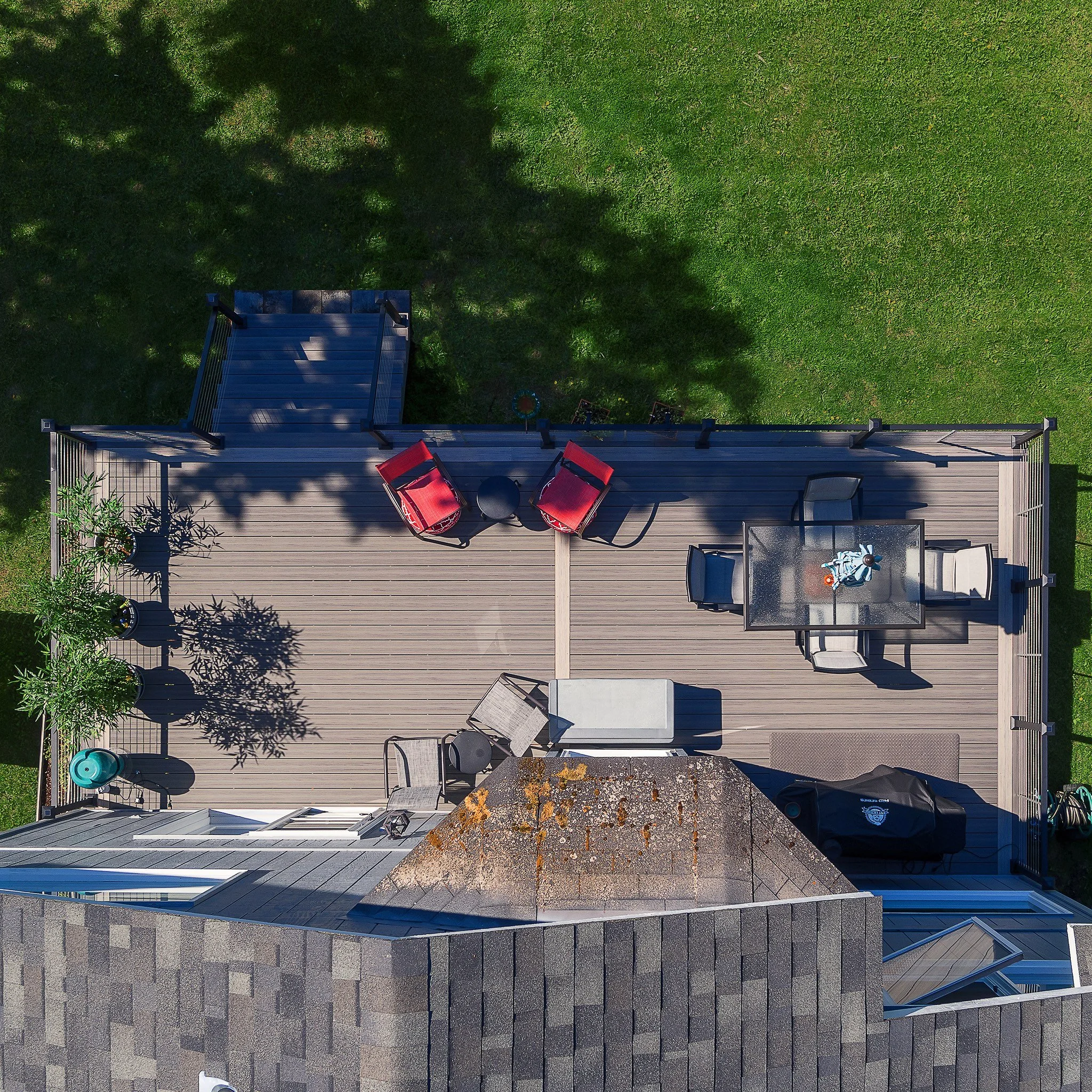 An overhead view of a composite deck attached to a house. The deck features outdoor furniture including two red chairs, a glass table with a decorative item, two modern chairs, and a lounge chair.