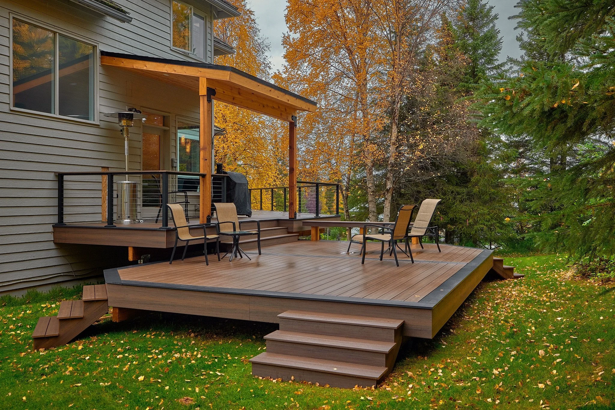 A composite deck attached to a house with stairs leading down to a grassy yard, surrounded by trees with fall foliage.