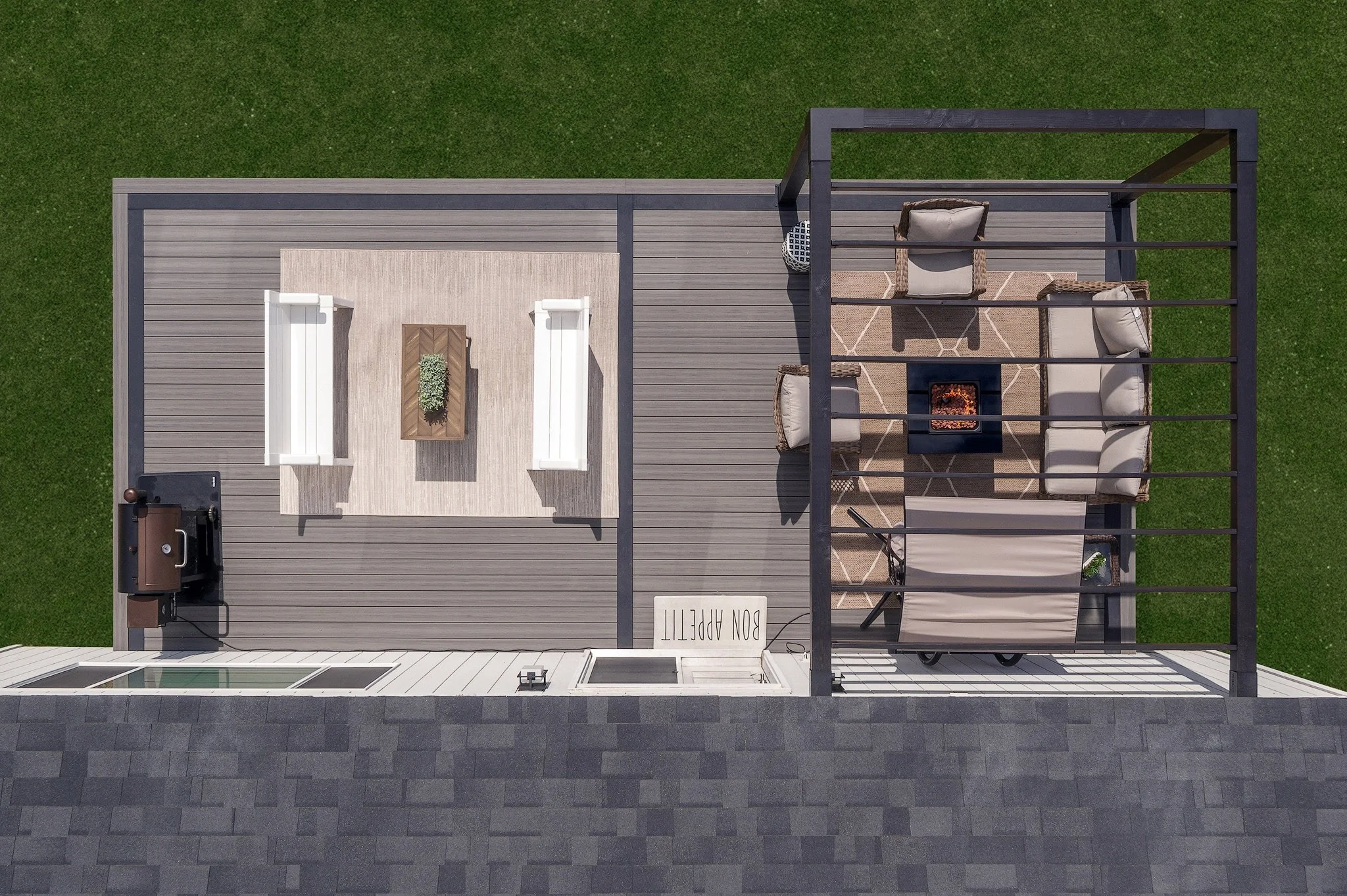 Overhead view of a backyard patio with outdoor furniture, a firepit, a grill, and a dining area with a barbecue, on a green lawn.