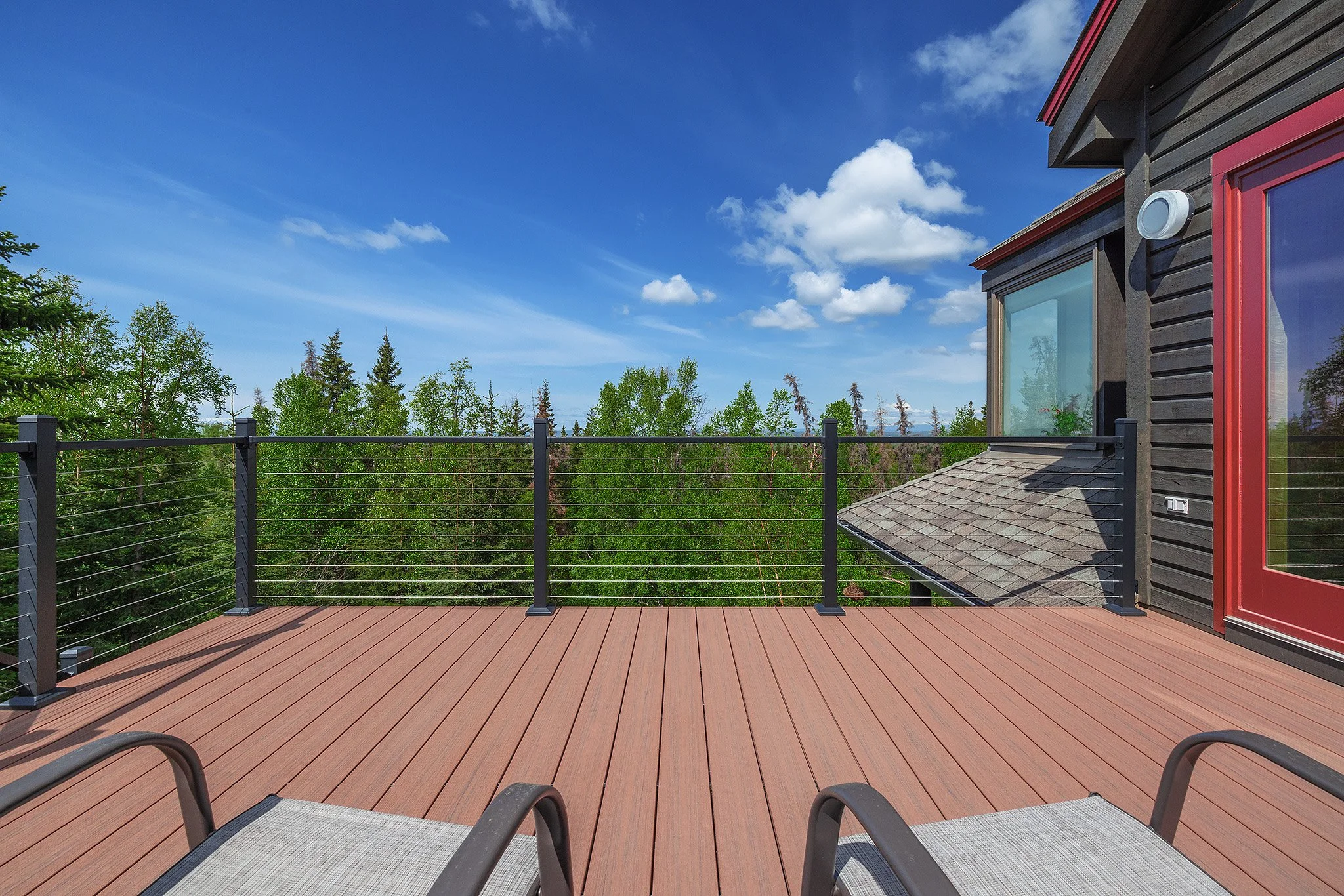View of a composite deck with metal railings overlooking green trees and a blue sky with clouds at a house.