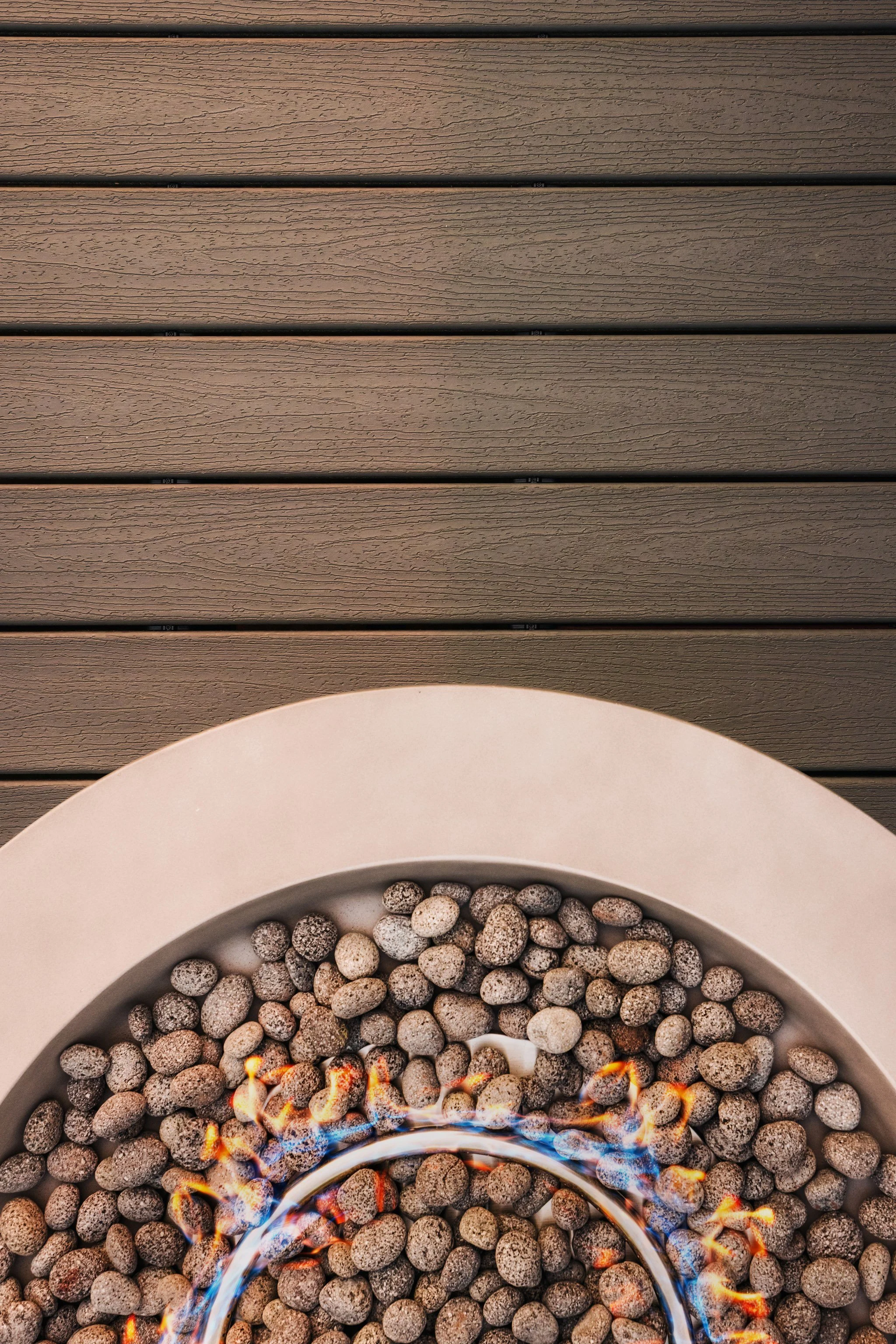 Top view of a heating fire pit filled with small stones on a trex deck.