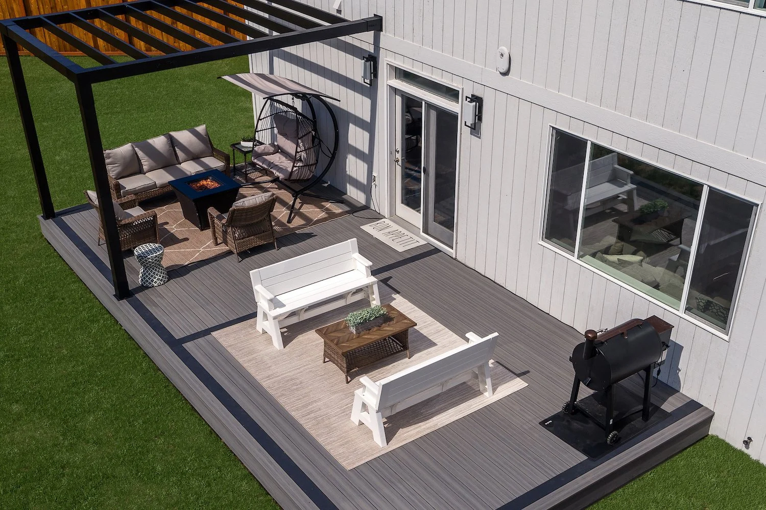A backyard patio featuring outdoor furniture, a grill, and a fire pit, adjacent to a house with large windows and a door.