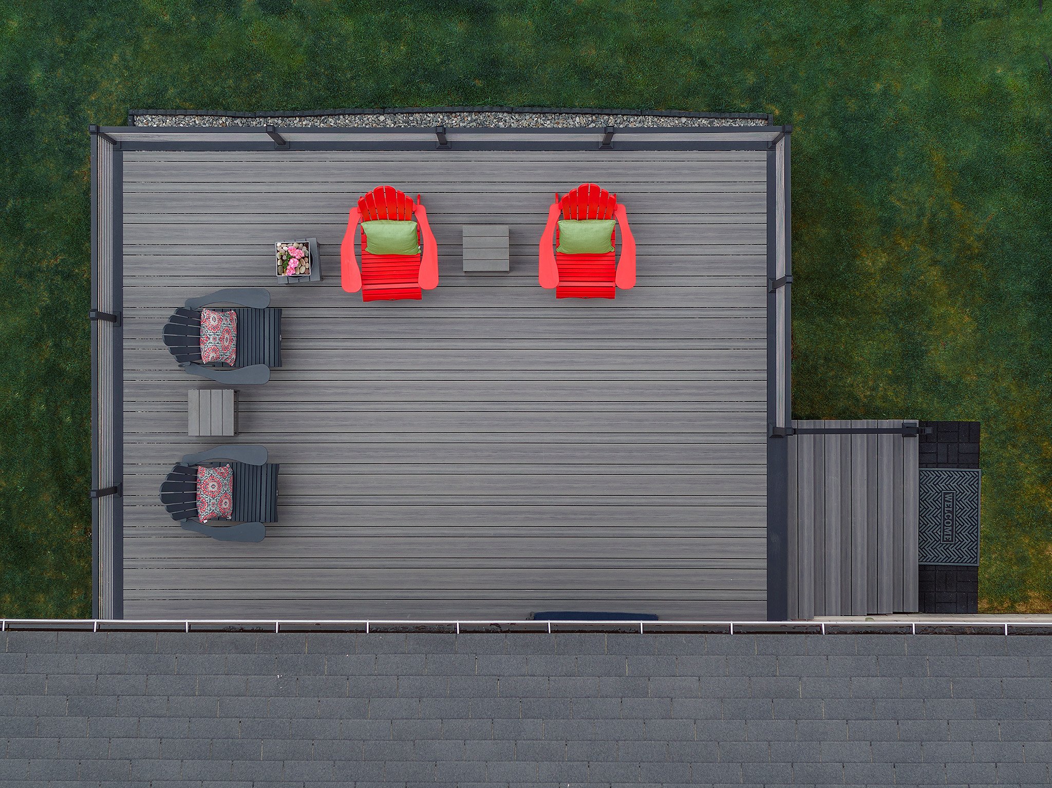 Aerial view of a composite deck with two red Adirondack chairs with green cushions, two gray Adirondack chairs with cushions, small tables, and potted flowers, surrounded by a grassy yard.