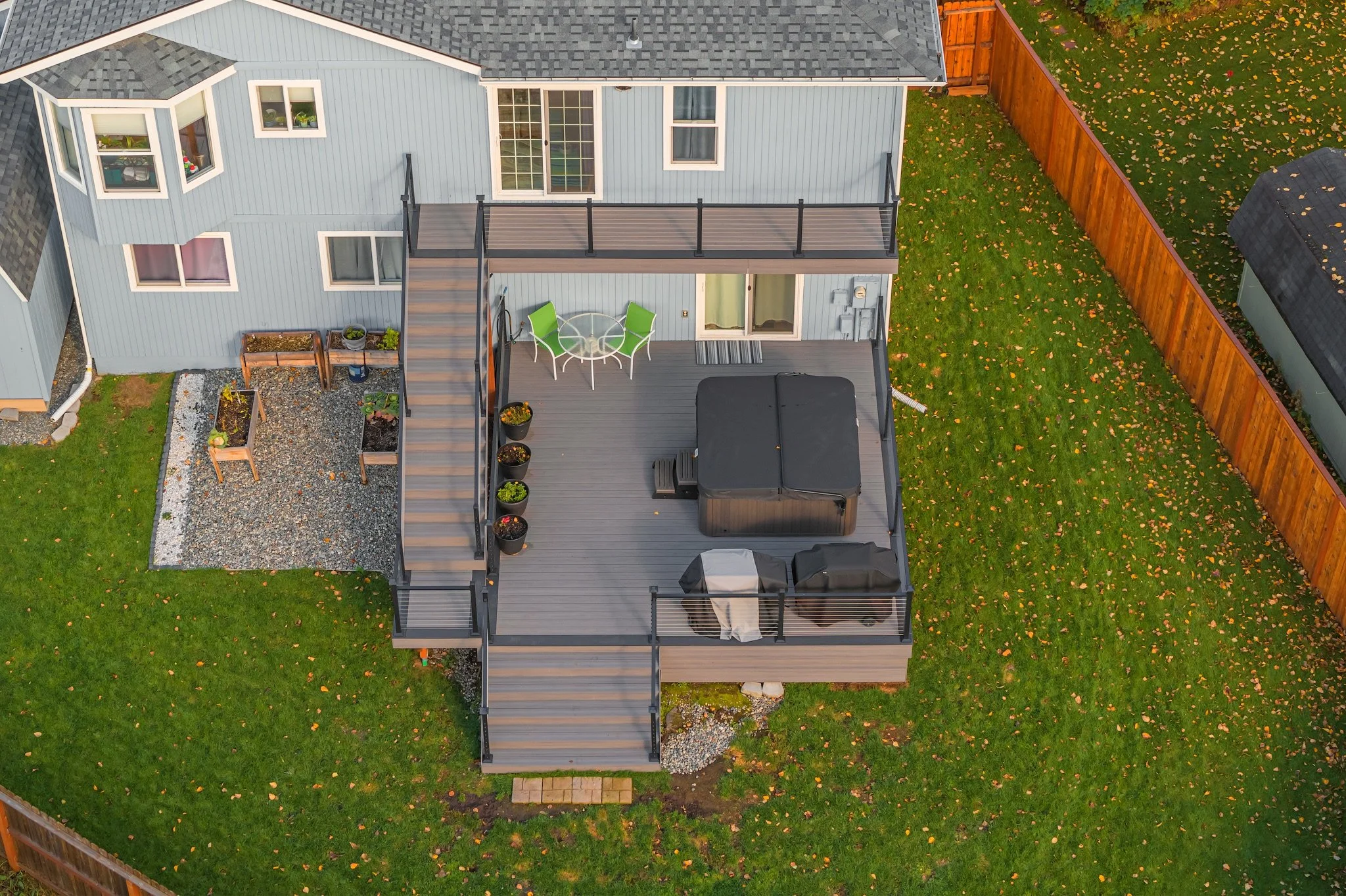 Aerial view of a backyard with a composite deck, outdoor furniture, potted plants, and a lawn with fallen leaves, surrounded by a wooden fence.