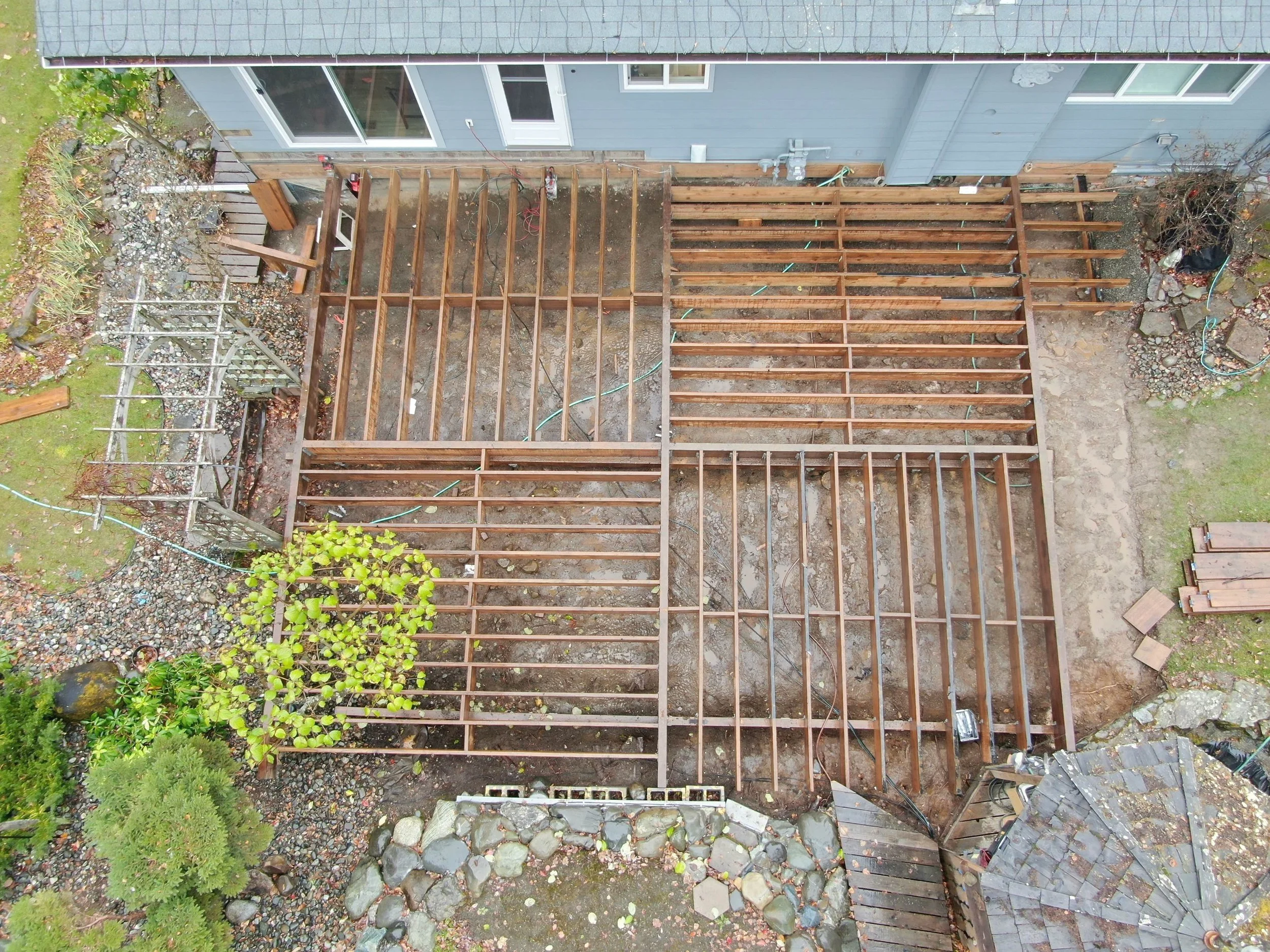 Aerial view of a house with a partially constructed wooden deck in the backyard, surrounded by grass, plants, and stones.