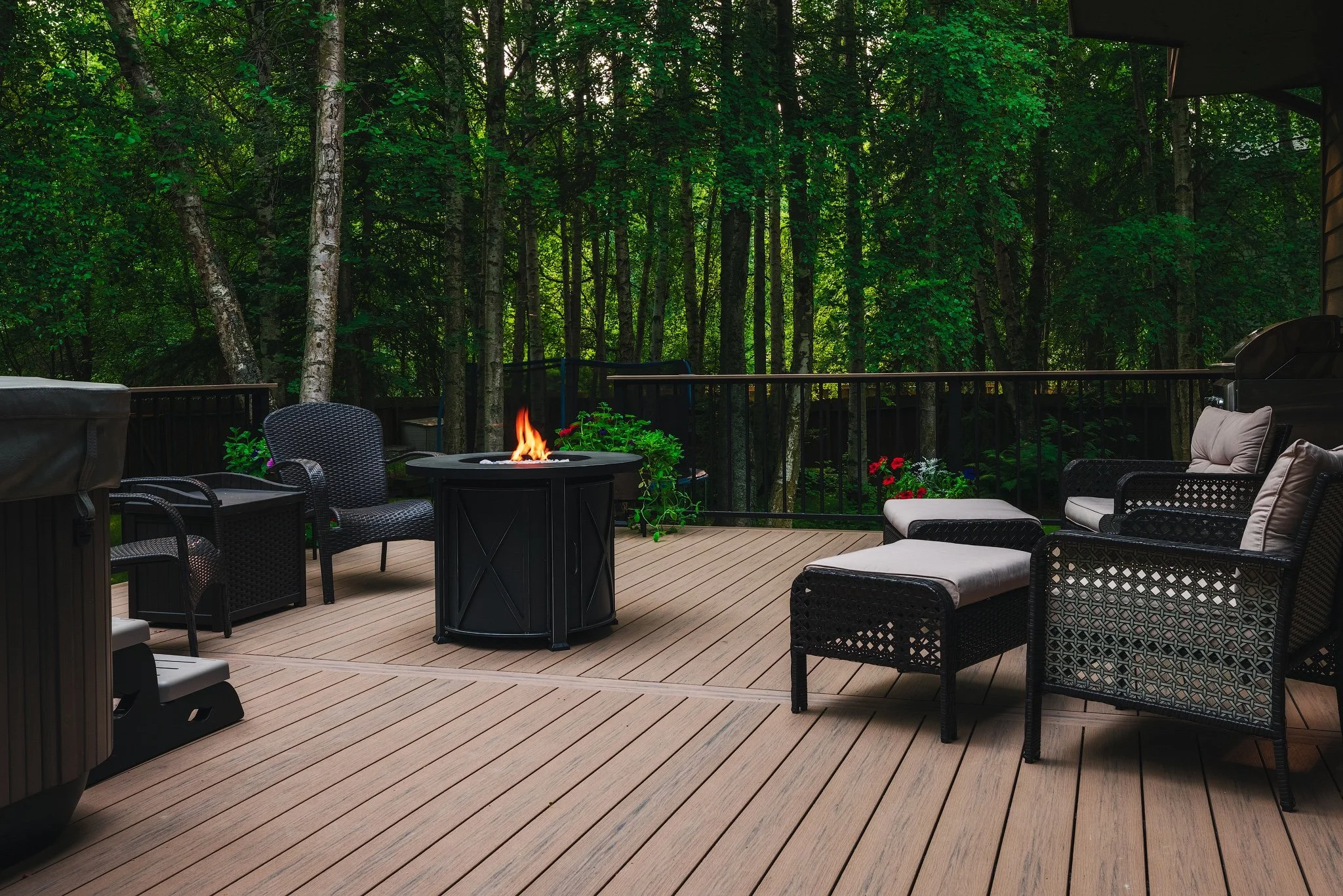 Outdoor deck with patio furniture and fire pit, surrounded by trees and greenery.