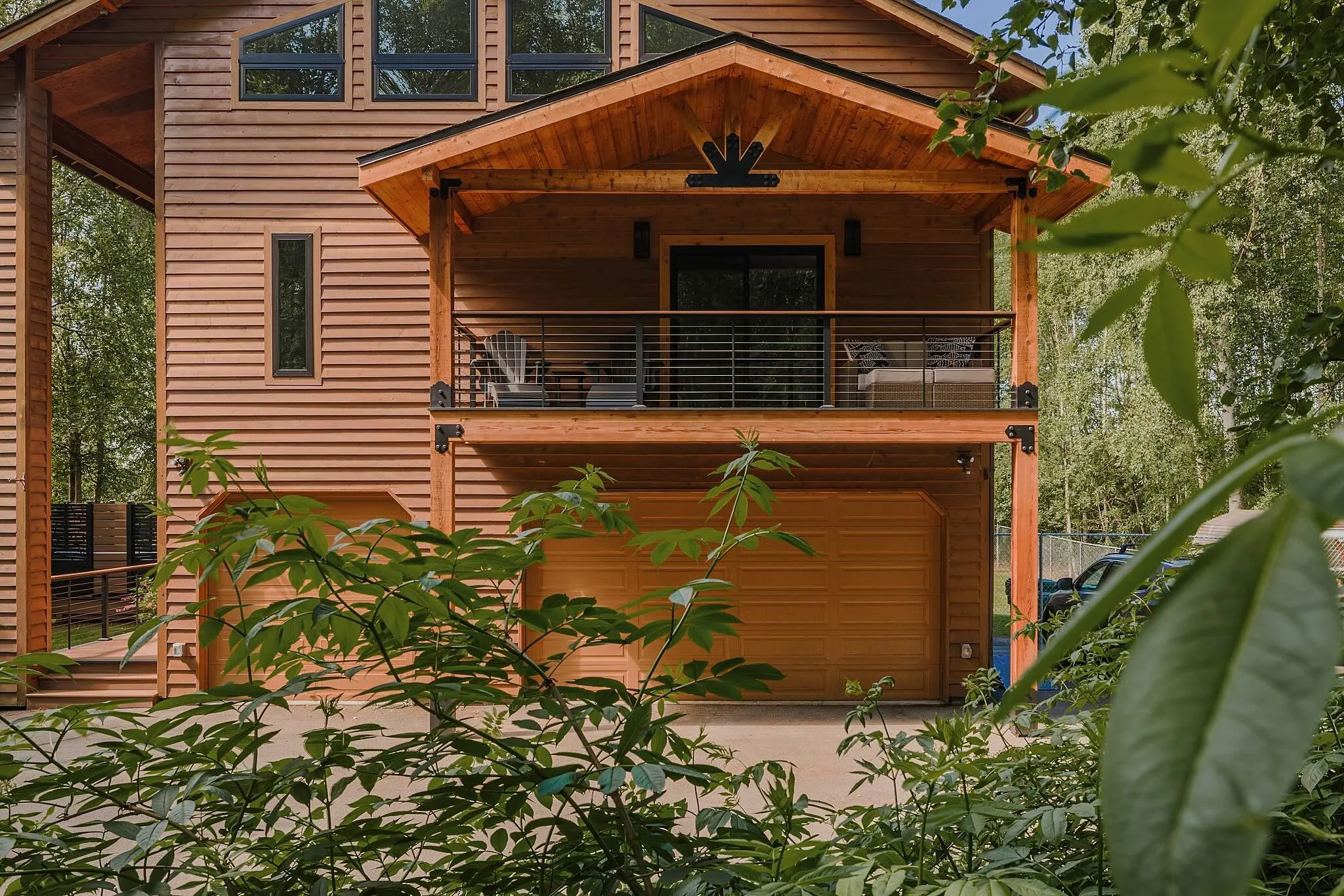 A two-story wooden house with a front balcony, surrounded by greenery and trees.