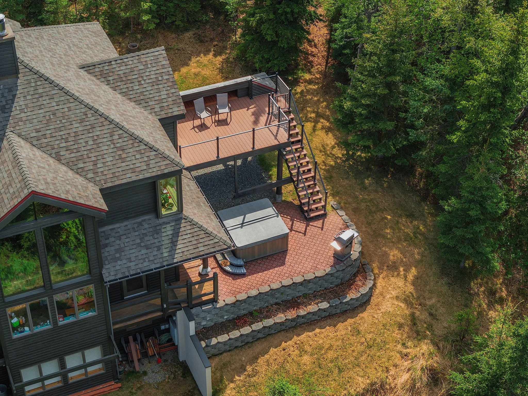 Aerial view of a house with a backyard deck, barbecue grill, and garden furniture, surrounded by trees and grass.