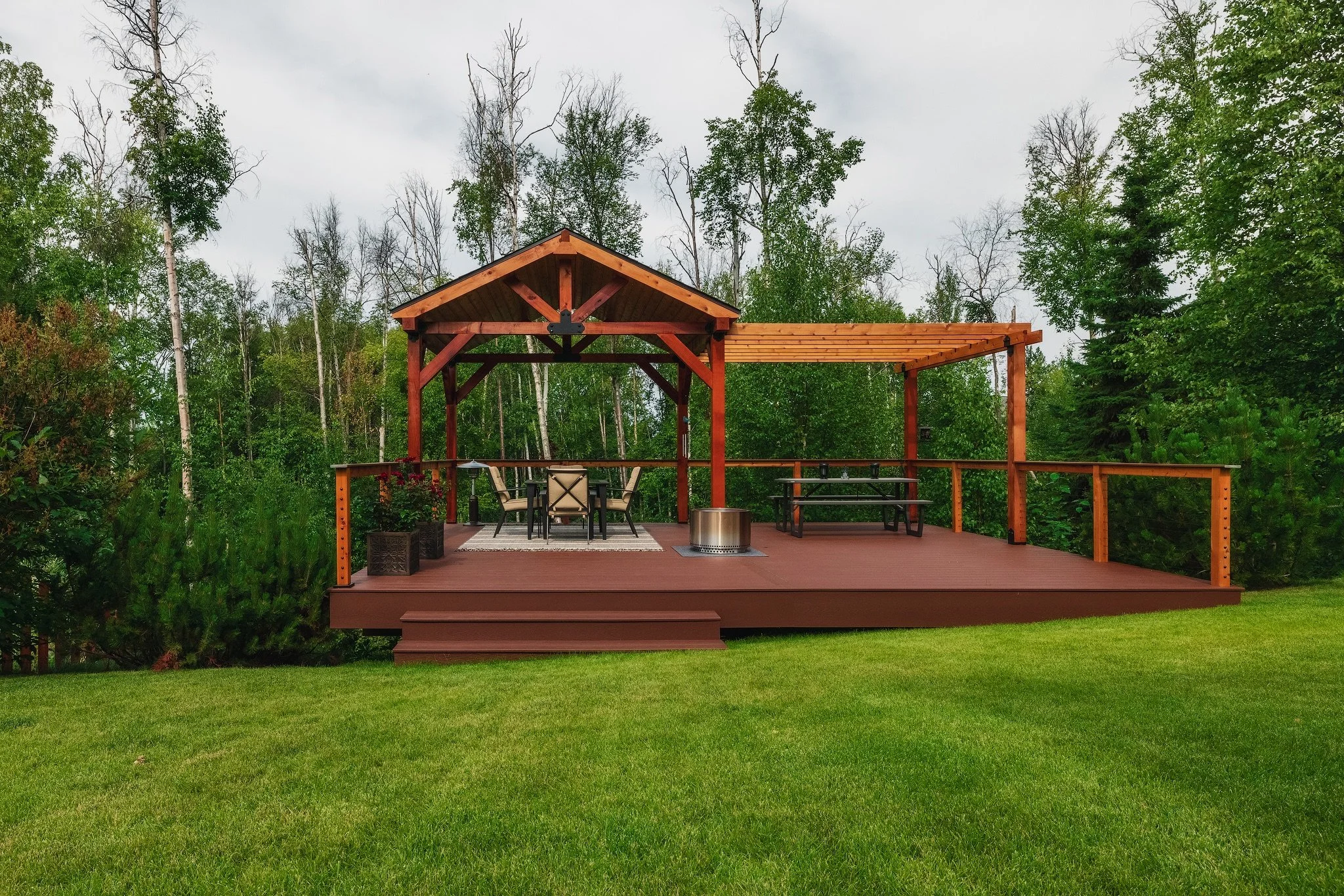 A trex deck with a gazebo, patio furniture, and a grassy yard surrounded by trees.